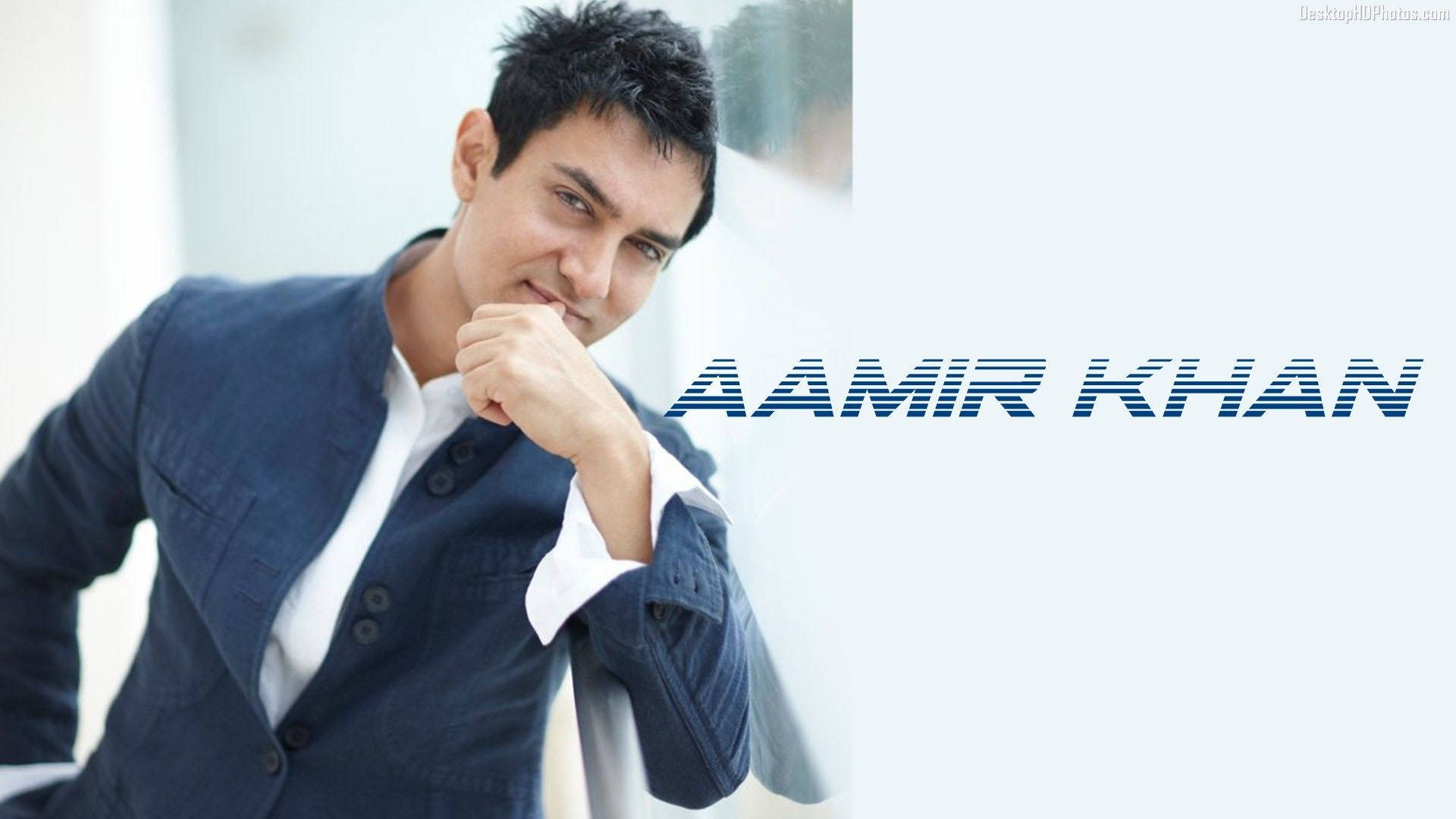 Aamir Khan 桌布 壁紙 — 阿米爾·汗身穿海軍藍西裝外套和白色襯衫，在明亮的極簡背景前，自信地將手放在下巴附近擺姿勢。