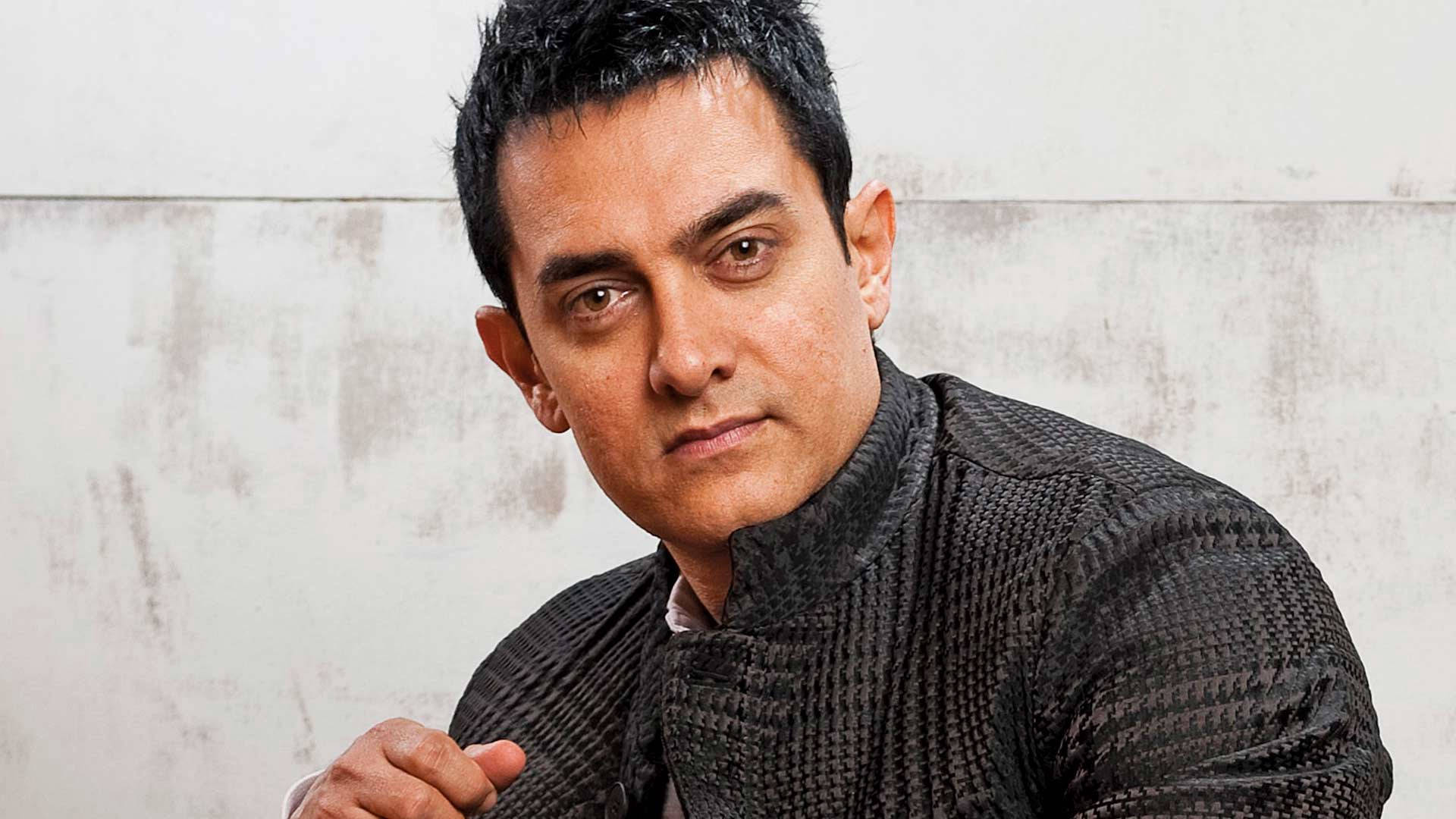 Aamir Khan 桌布 壁紙 — 阿米爾汗身穿質感黑色襯衫，在風化的白色牆壁前以嚴肅的眼神擺姿勢。