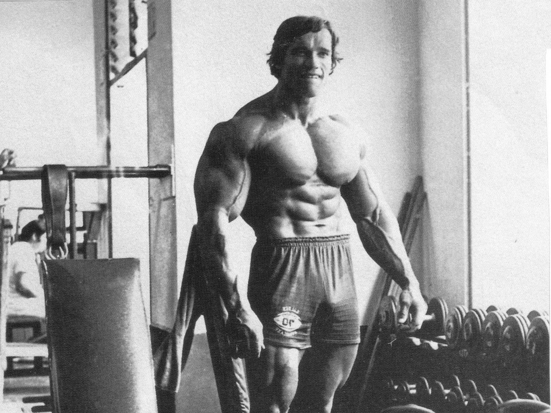 Arnold 桌布 壁紙 — 阿諾·史瓦辛格在一張復古黑白健身房照片中展示他肌肉發達的身材。