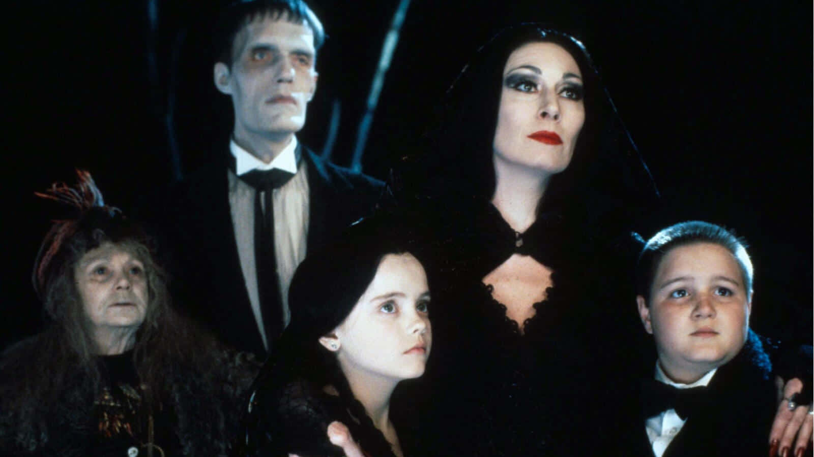 Addams Family 桌布 壁紙 — 阿達一族以哥德式黑色服裝在黑暗背景下擺姿勢，燈光效果戲劇性。
