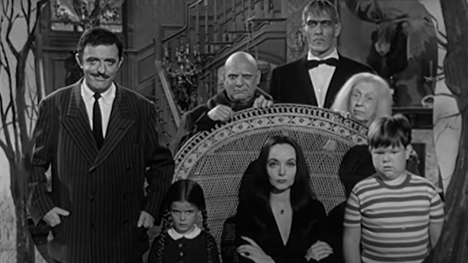 Addams Family 桌布 壁紙 — 阿達一族在他們的哥德式豪宅中莊嚴地擺姿勢，周圍是華麗的家具和詭異的裝飾。