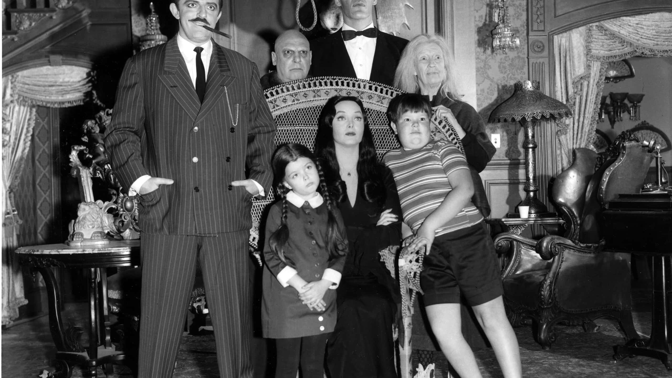 Addams Family 桌布 壁紙 — 阿達一族在他們華麗的哥德式客廳中擺姿勢，配有復古家具和戲劇性的表情。