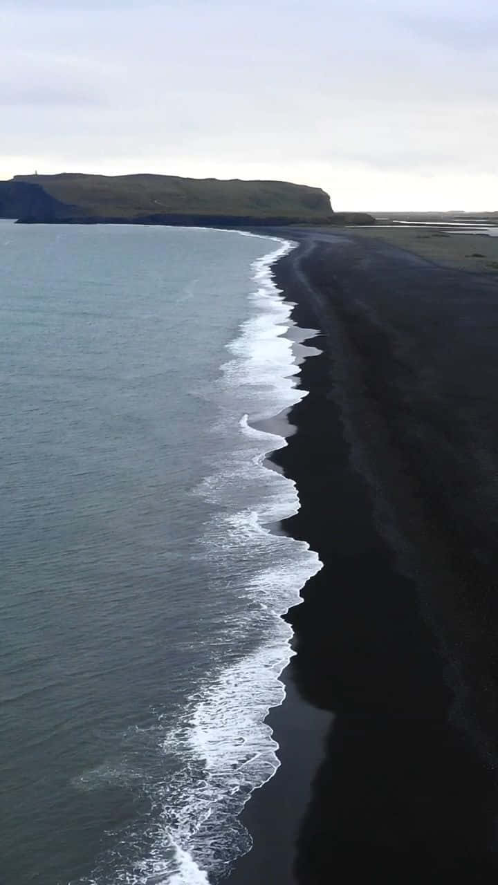 Winter Beach 桌布 壁紙 — 陰天下一片荒涼的黑沙灘鳥瞰圖，泡沫般的海浪拍打著海岸。