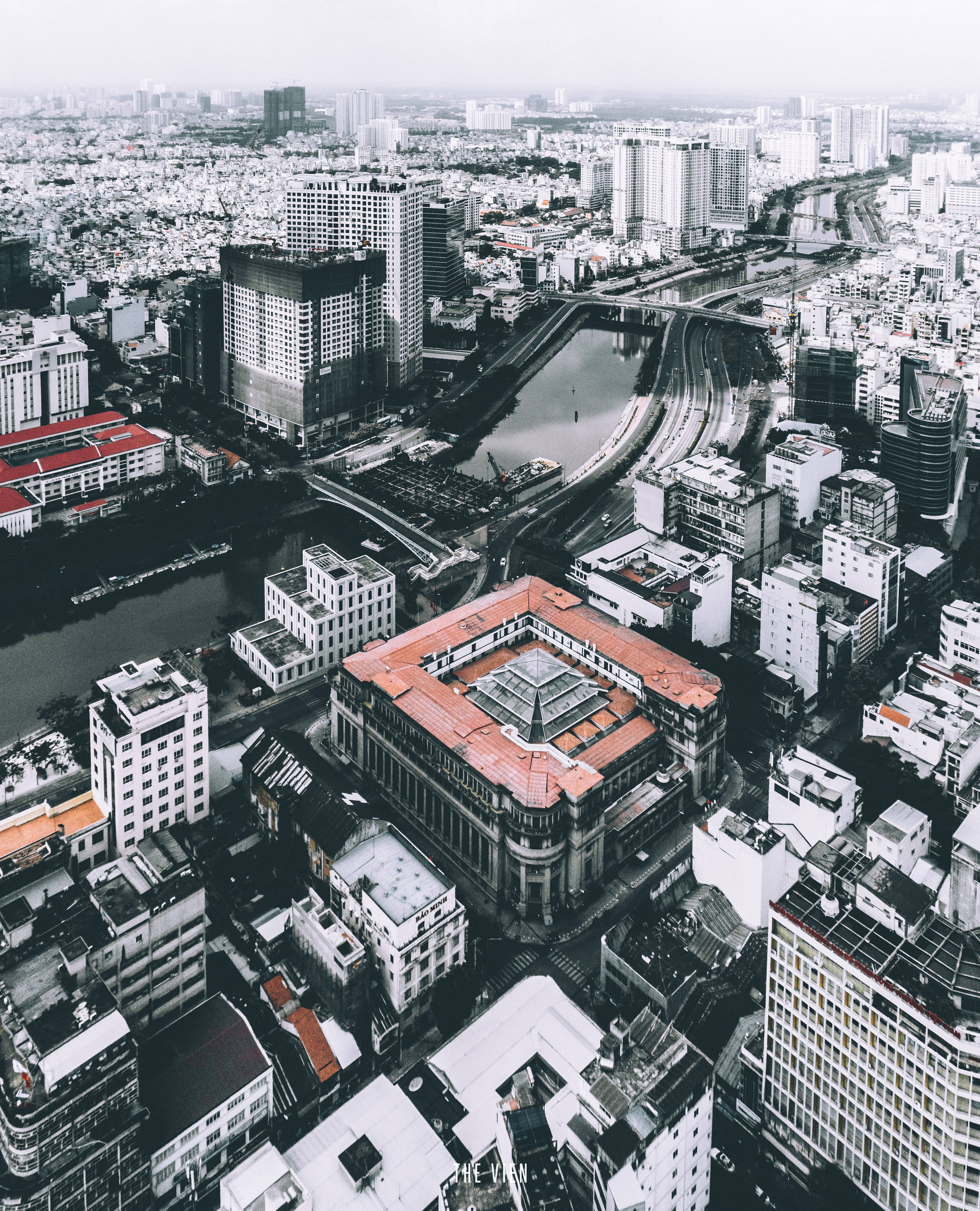 Ho Chi Minh City 桌布 壁紙 — 陰天天空下，一條蜿蜒的河流穿過現代和傳統建築的密集城市景觀的鳥瞰圖。