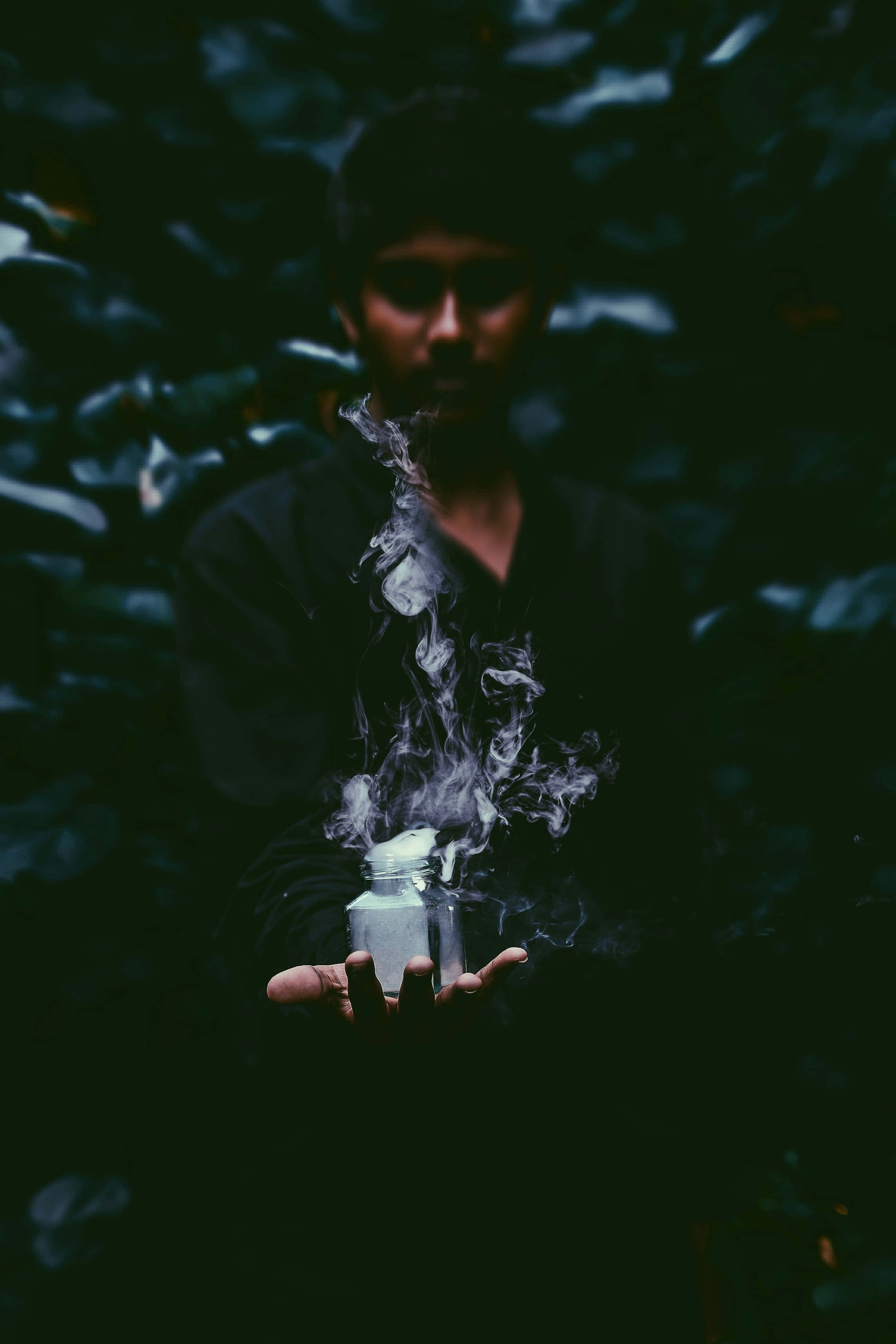 Indian 桌布 壁紙 — 陰影中的人手持冒煙的罐子，置身於黑暗的樹葉中，營造出陰鬱的森林場景。