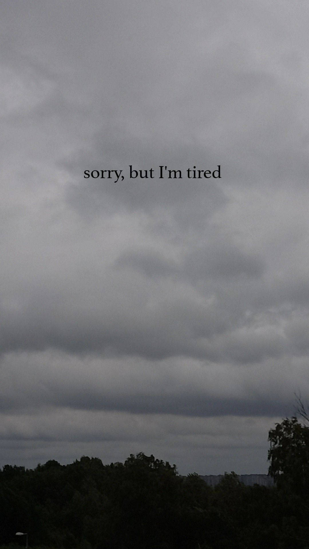 tired 桌布 壁紙 — 陰沉的灰色天空，烏雲密佈，籠罩著樹木的剪影，中央有文字「sorry but I'm tired」。