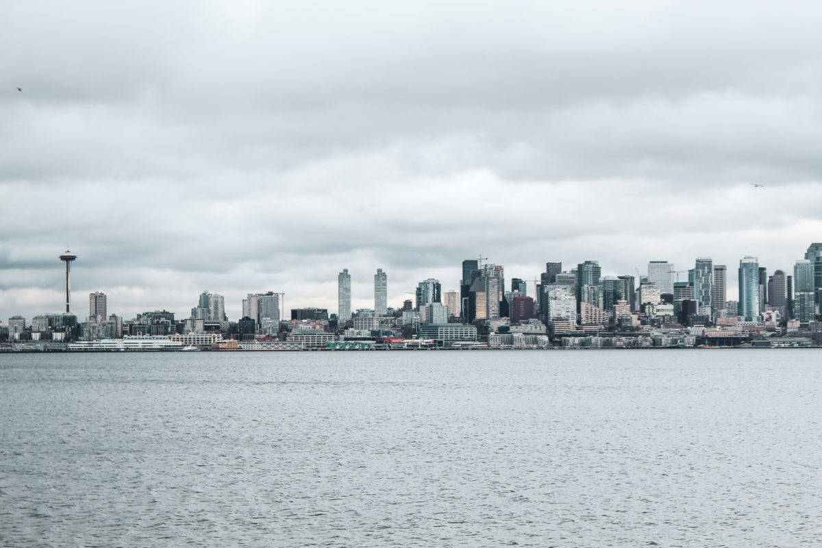 Seattle Skyline 桌布 壁紙 — 陰沉的烏雲籠罩著西雅圖標誌性的天際線，太空針塔高聳於現代摩天大樓旁，倒映在平靜的水面上。