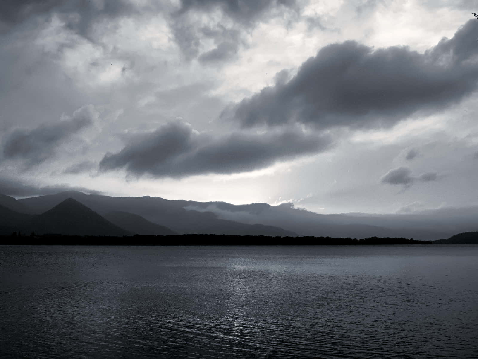 Black And White Cloud 桌布 壁紙 — 陰鬱的湖面映照著遠處山巒剪影上方昏暗暮光下的黑暗風暴雲。