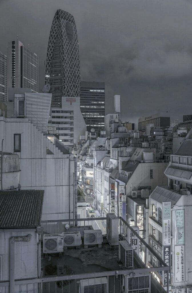 灰色美學動圖 桌布 壁紙 — 陰鬱的黑白城市夜景，密集建築物上方聳立著格子狀摩天大樓，街燈閃爍。