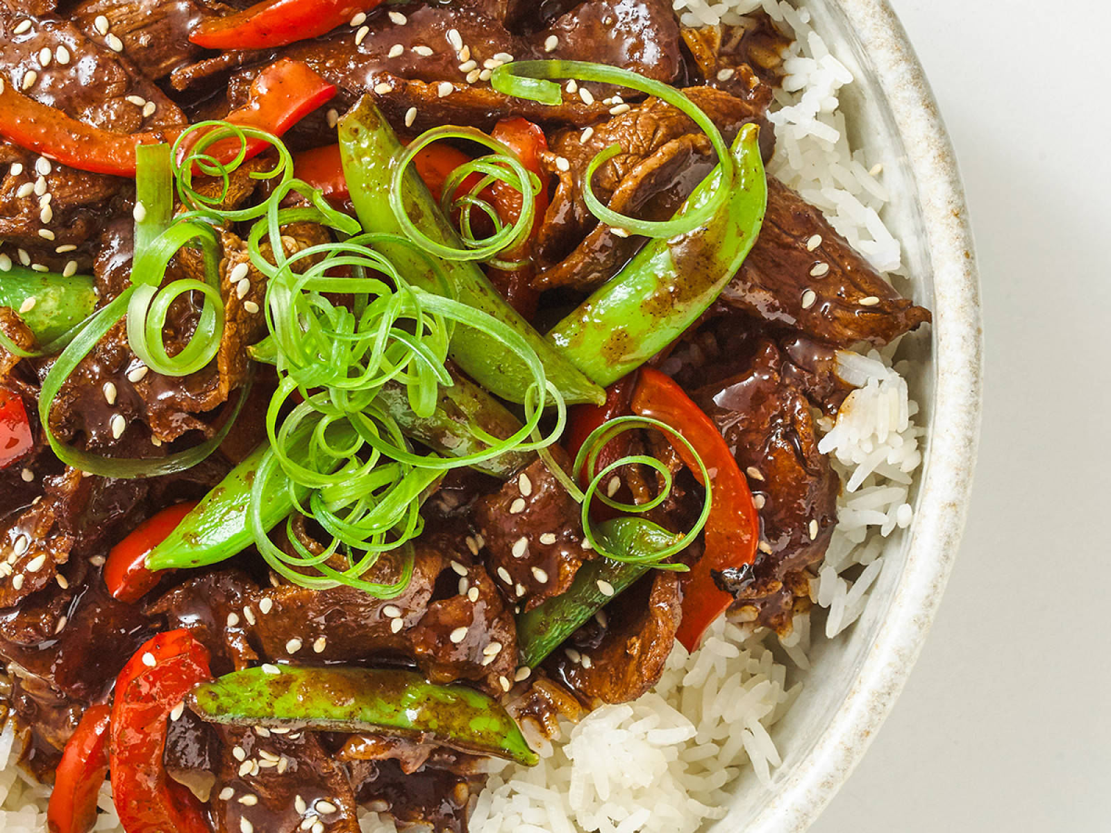 Rice 桌布 壁紙 — 陶瓷碗中白飯上的牛肉蔬菜炒菜近距離特寫，有紅椒、青荷蘭豆和芝麻。