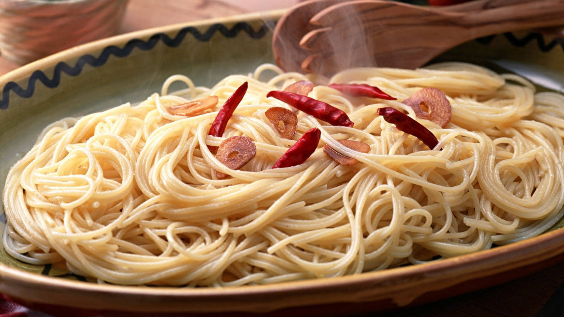 Pasta 桌布 壁紙 — 陶瓷碗中盛載著冒煙的義大利麵，上面放有紅辣椒和蒜瓣，搭配木匙。