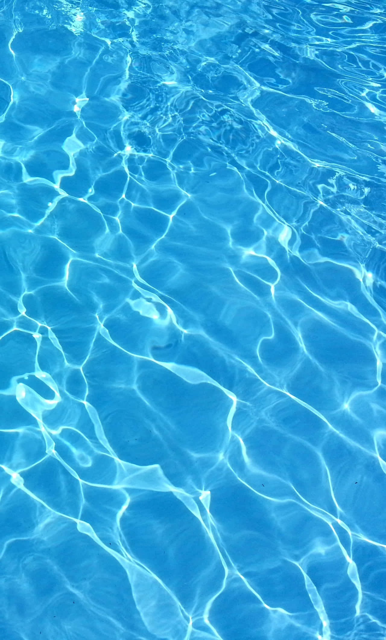 Pool Water 桌布 壁紙 — 陽光在水晶般清澈的藍色水面上舞動，形成閃爍的光影圖案。