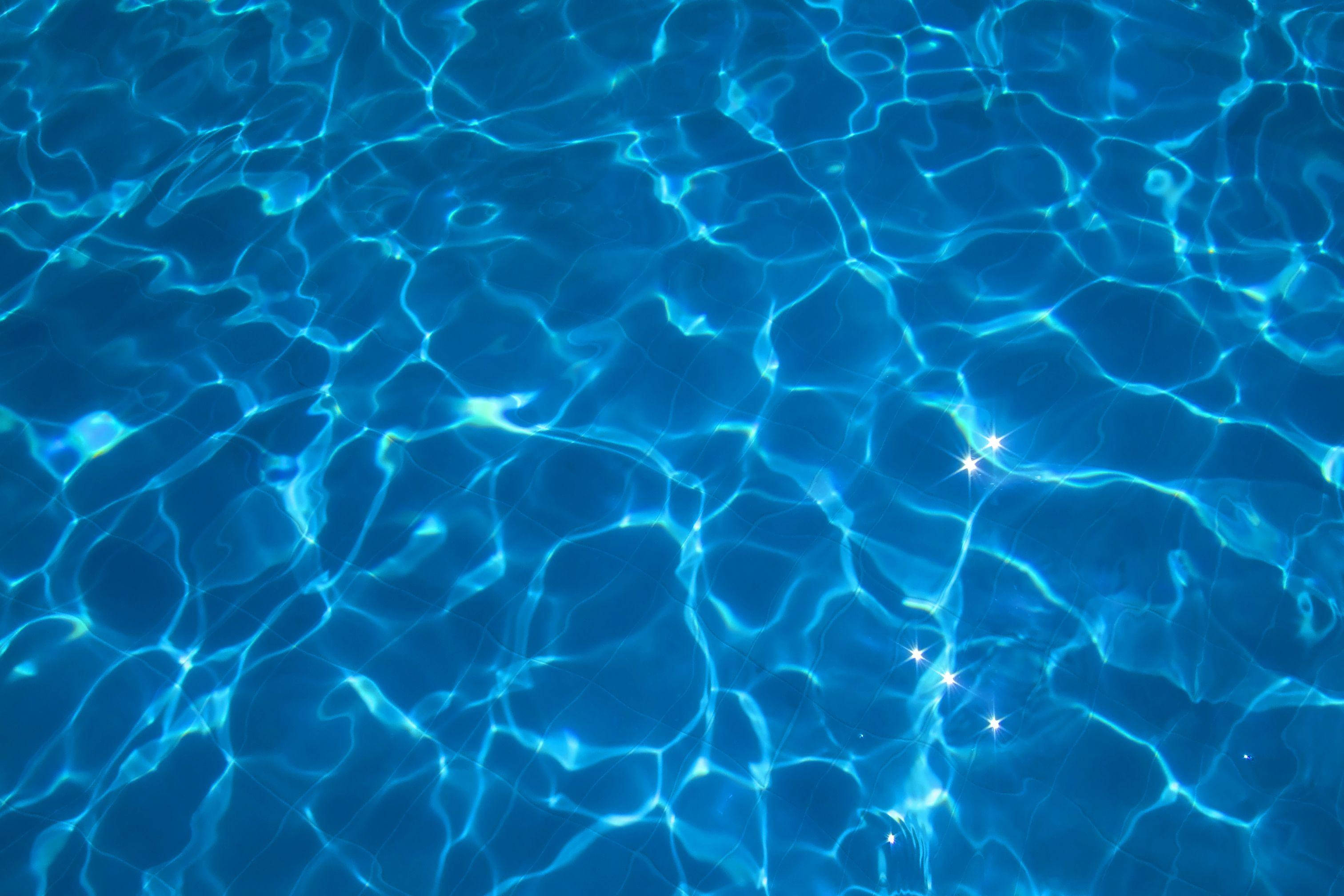 Water Aesthetic 桌布 壁紙 — 陽光在泛起漣漪的藍色泳池水面上舞動，形成閃爍的圖案和發光的高光。