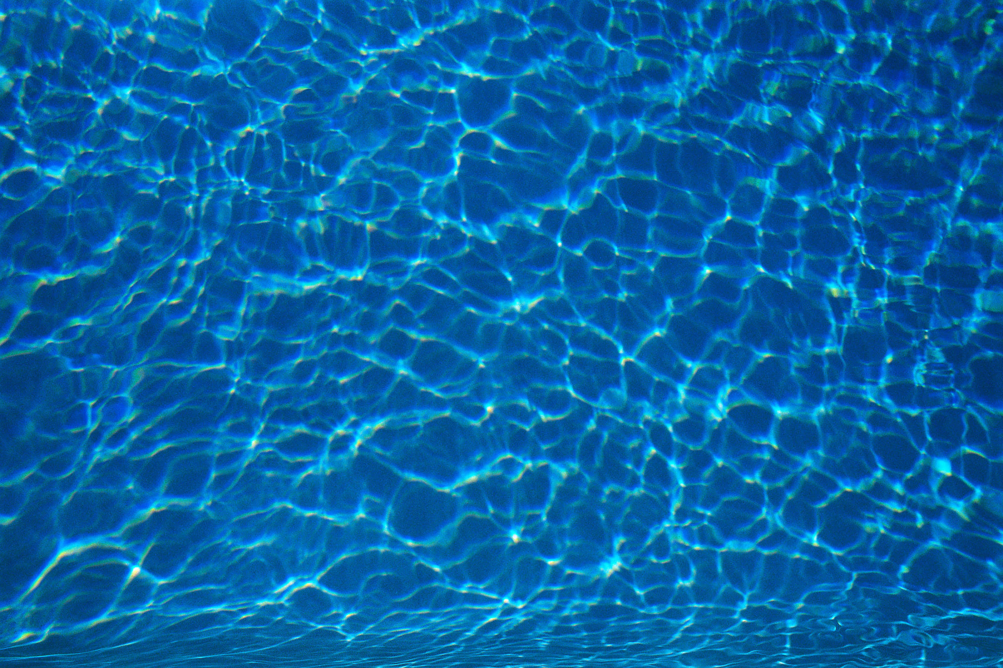 Water Texture 桌布 壁紙 — 陽光在波光粼粼的藍色泳池水面上舞動，形成迷人的光影圖案。