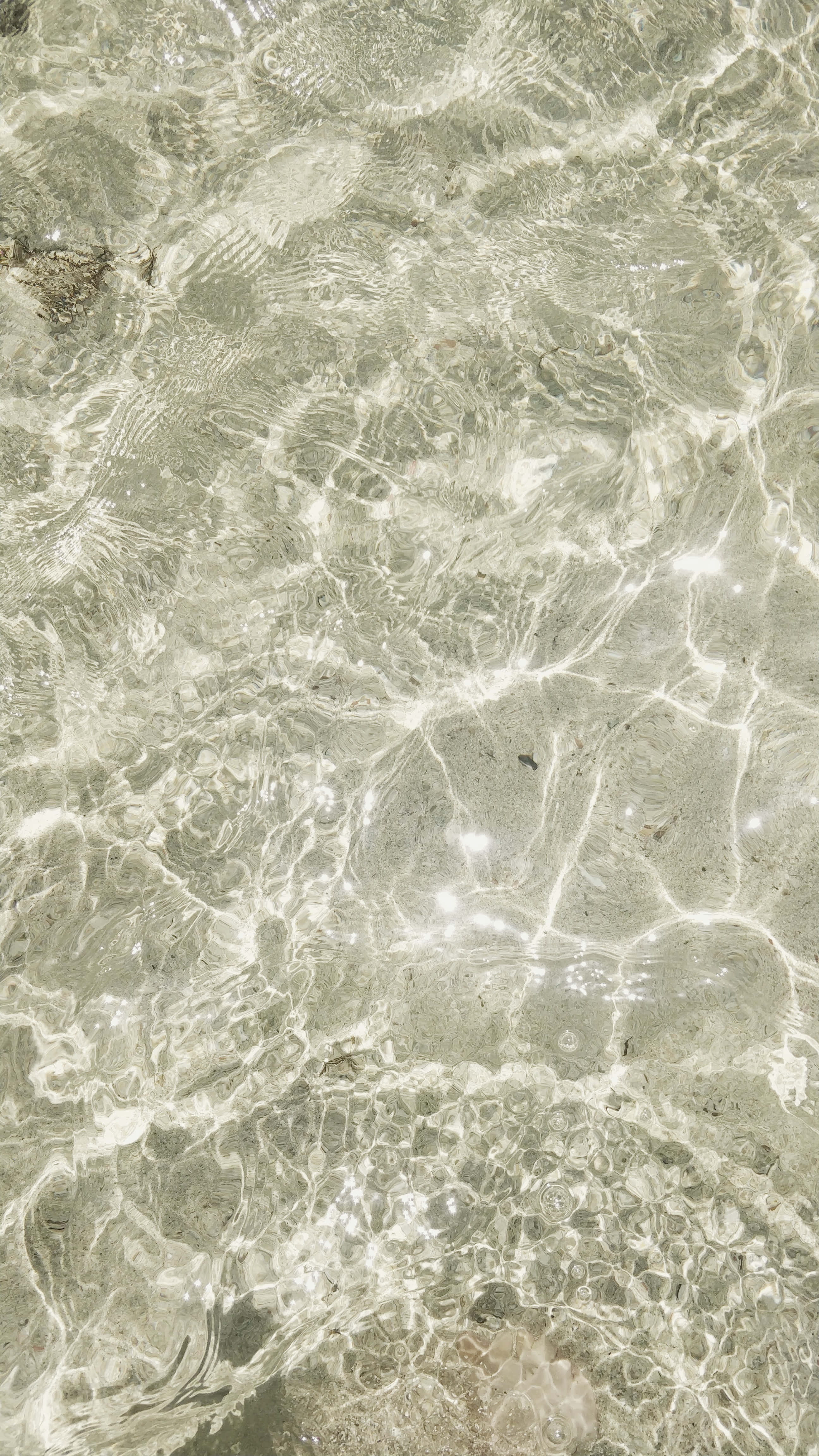 Marble iPad 桌布 壁紙 — 陽光在淺而清澈的水面上泛起漣漪，顯露出有紋理的沙質底部和散落的鵝卵石。