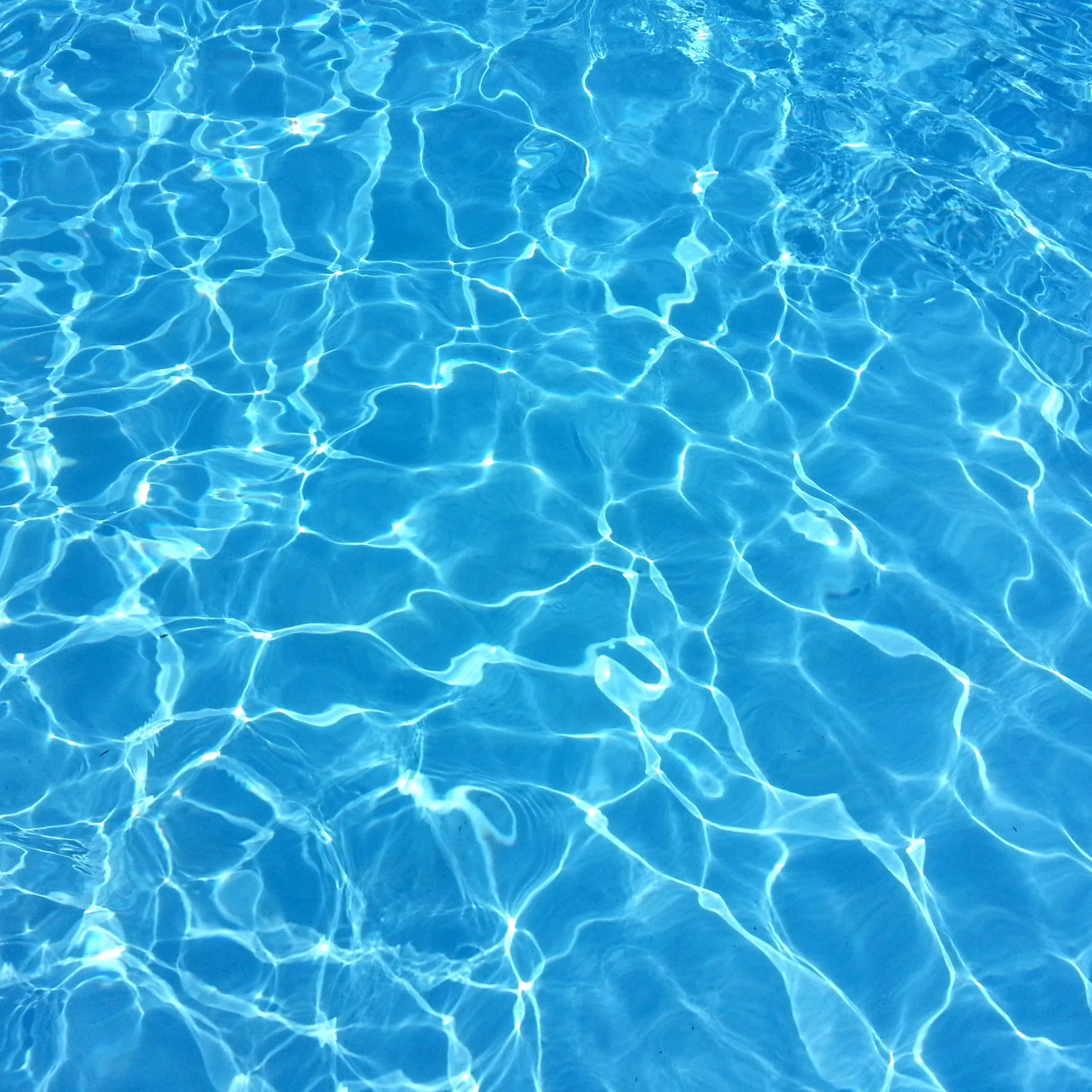 Water iPad 桌布 壁紙 — 陽光在清澈湛藍的泳池水面上舞動漣漪，形成閃爍的光影圖案。