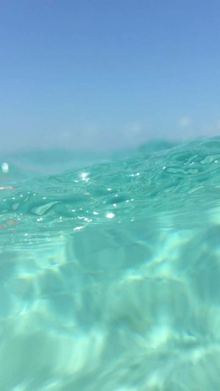 Cute Sea 桌布 壁紙 — 陽光在清澈藍天下的碧綠海浪上舞動，營造出寧靜的水下景觀。