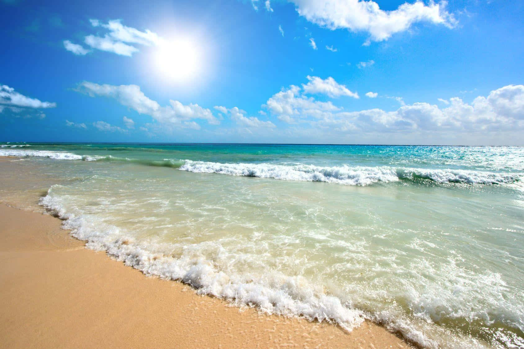 夏天 桌布 壁紙 — 陽光在碧綠色的海浪上閃爍，海浪拍打著金色的沙灘，天空湛藍，白雲朵朵。