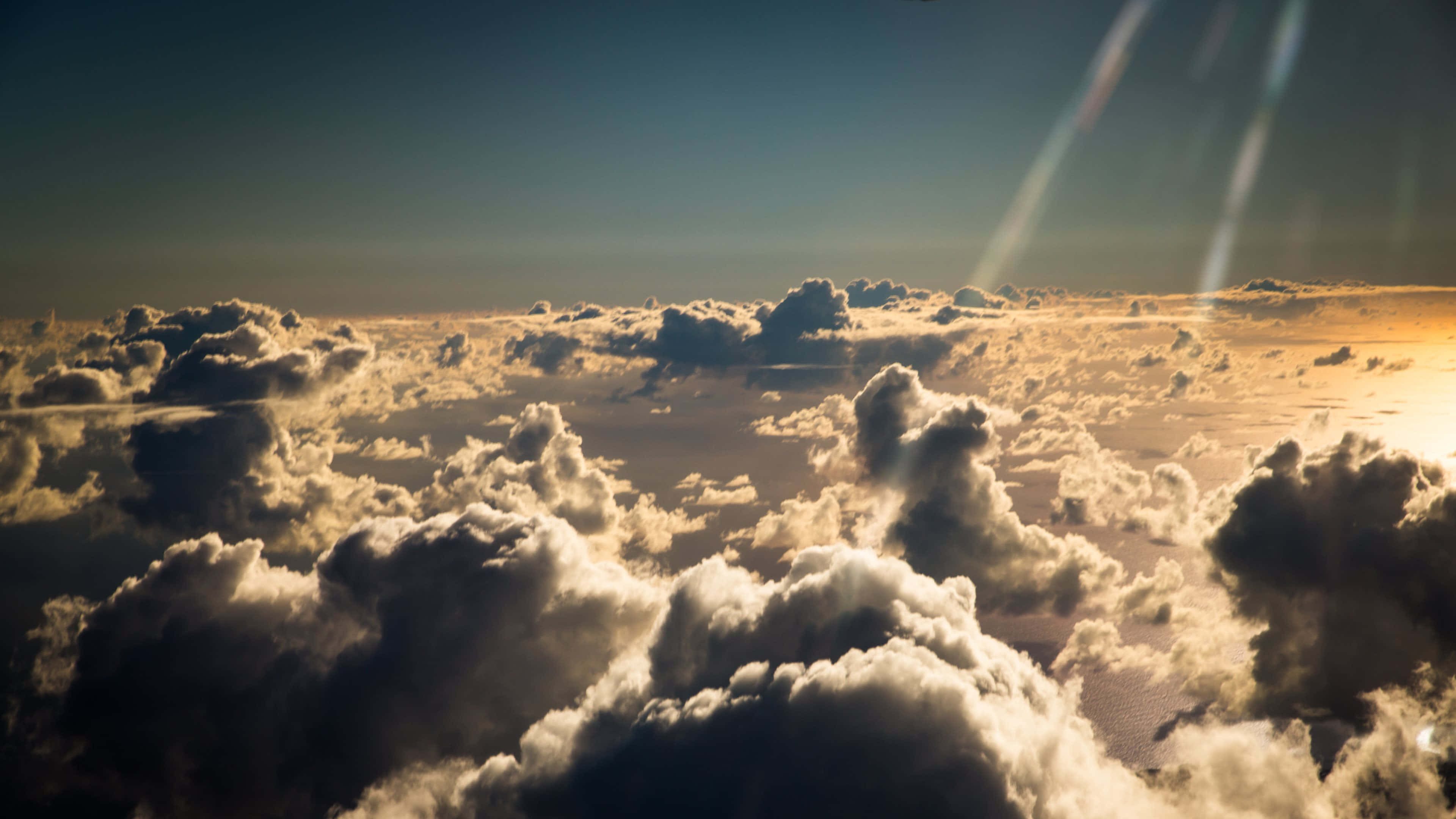 Clouds Aesthetics 桌布 壁紙 — 陽光從上方穿透金色雲層，在廣闊的蓬鬆雲海上形成戲劇性的光線。