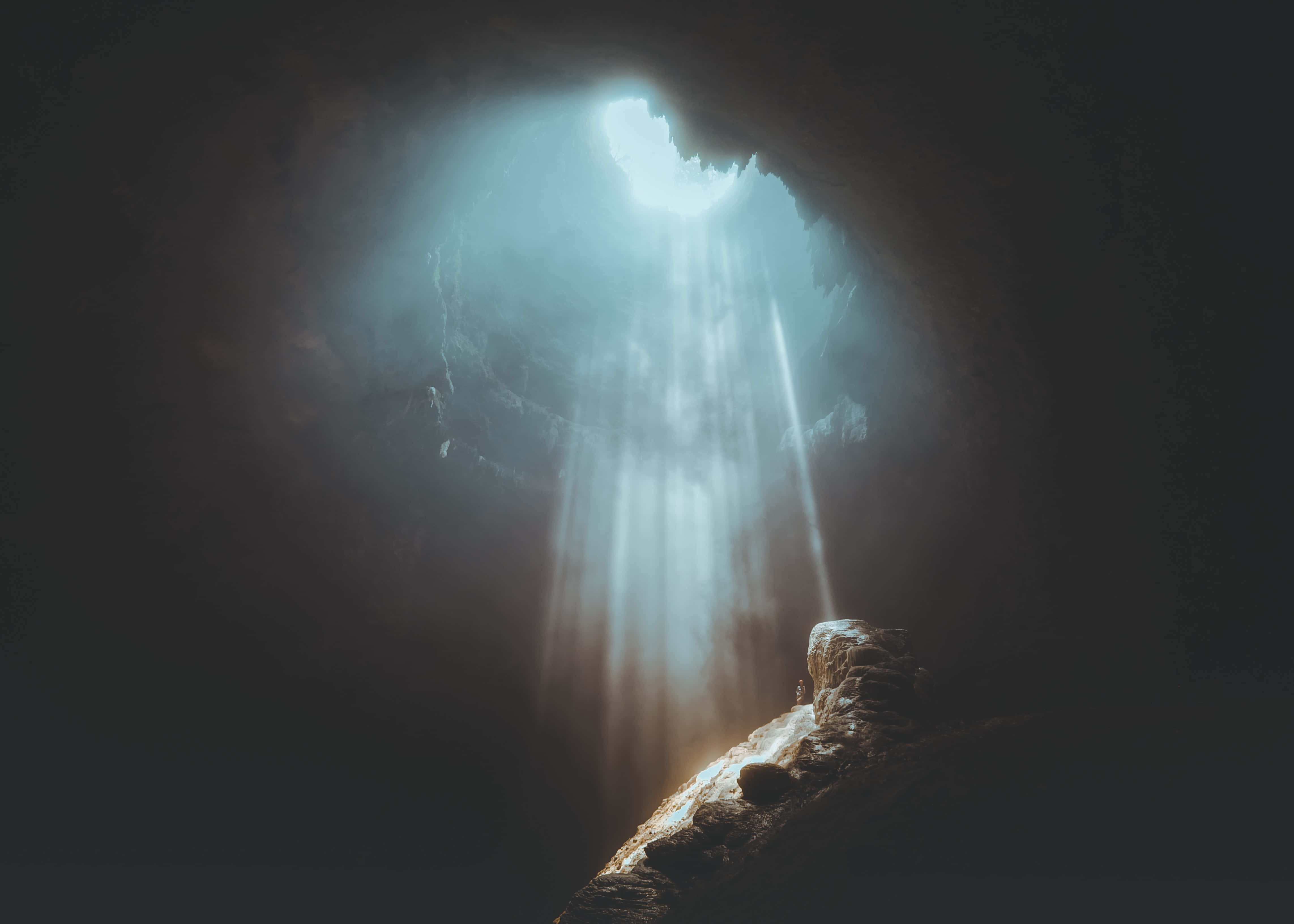 Cave 桌布 壁紙 — 陽光戲劇性地穿過洞穴開口，照亮下方的灰塵顆粒和崎嶇的岩石結構。
