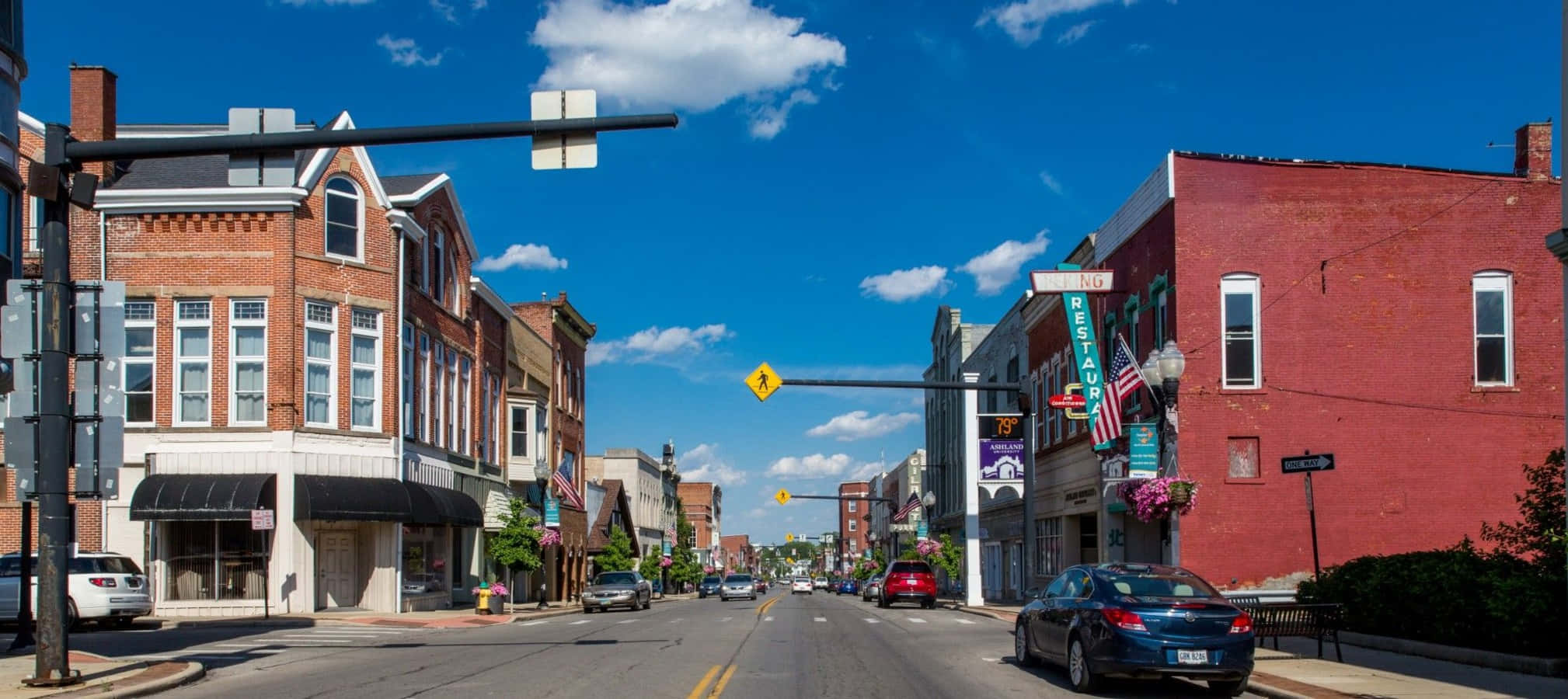 Ashland County 桌布 壁紙 — 陽光明媚的一天，在一條迷人的小鎮街道上，有磚砌建築、停放的汽車和晴朗的藍天，飄著蓬鬆的白雲。