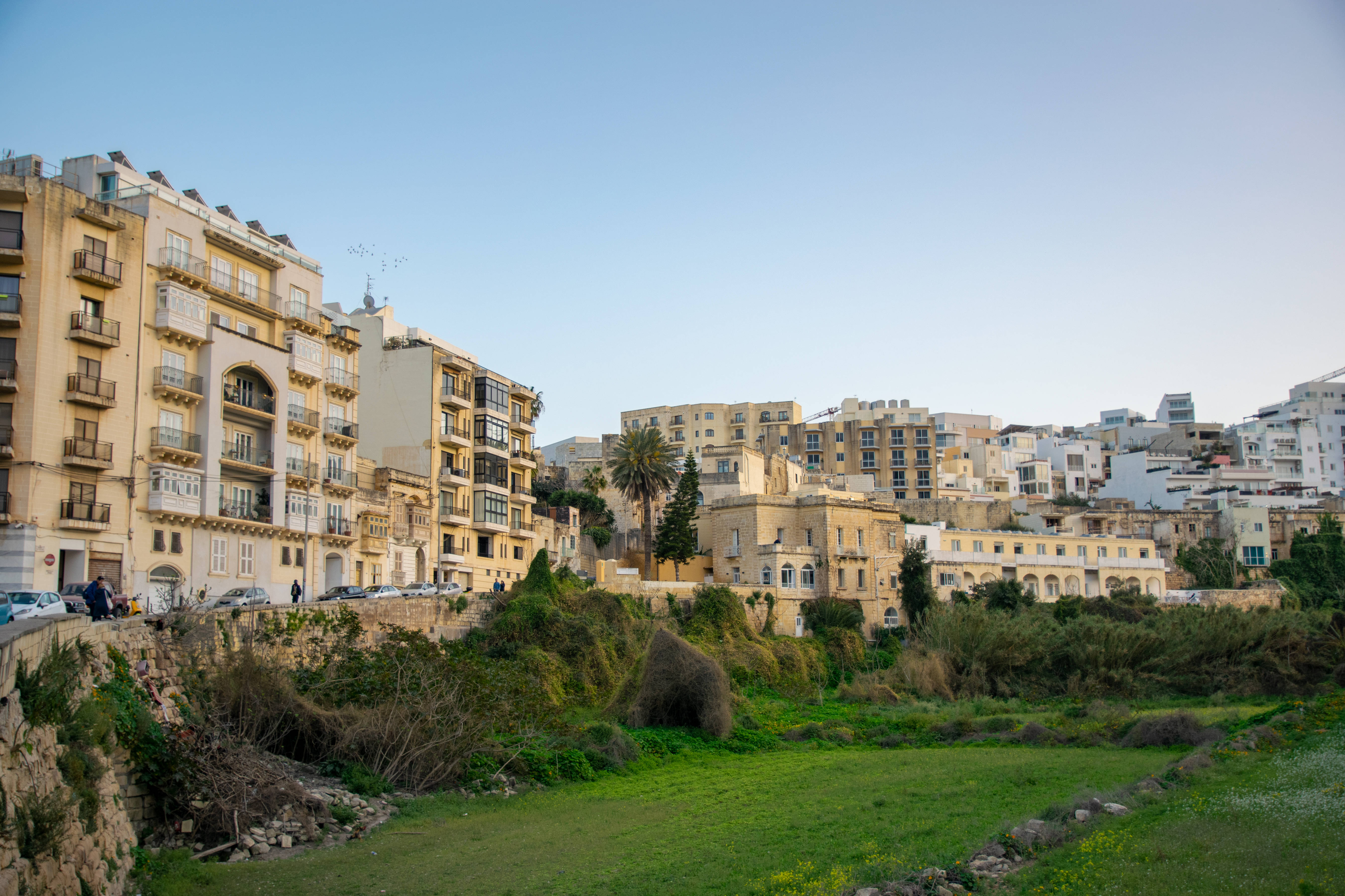 Malta 桌布 壁紙 — 陽光明媚的地中海小鎮，赤陶屋頂的建築沿著山坡向上延伸，俯瞰綠色山谷。