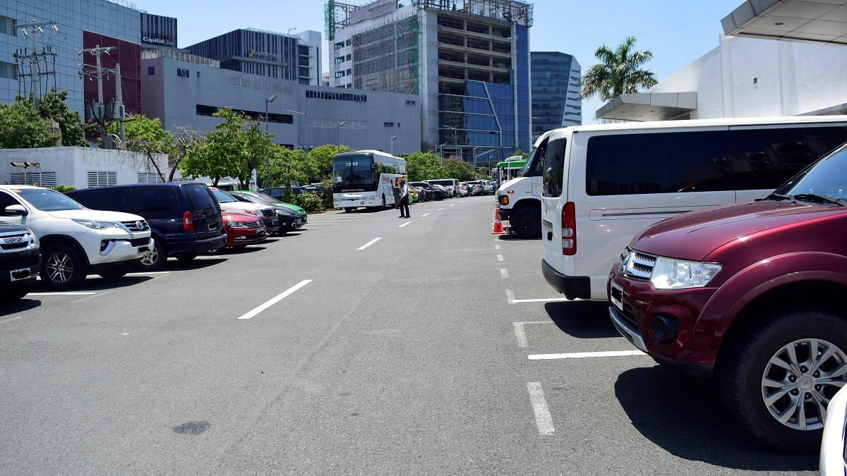 Road 桌布 壁紙 — 陽光明媚的城市停車場，停滿了汽車和巴士，背景是現代玻璃建築。