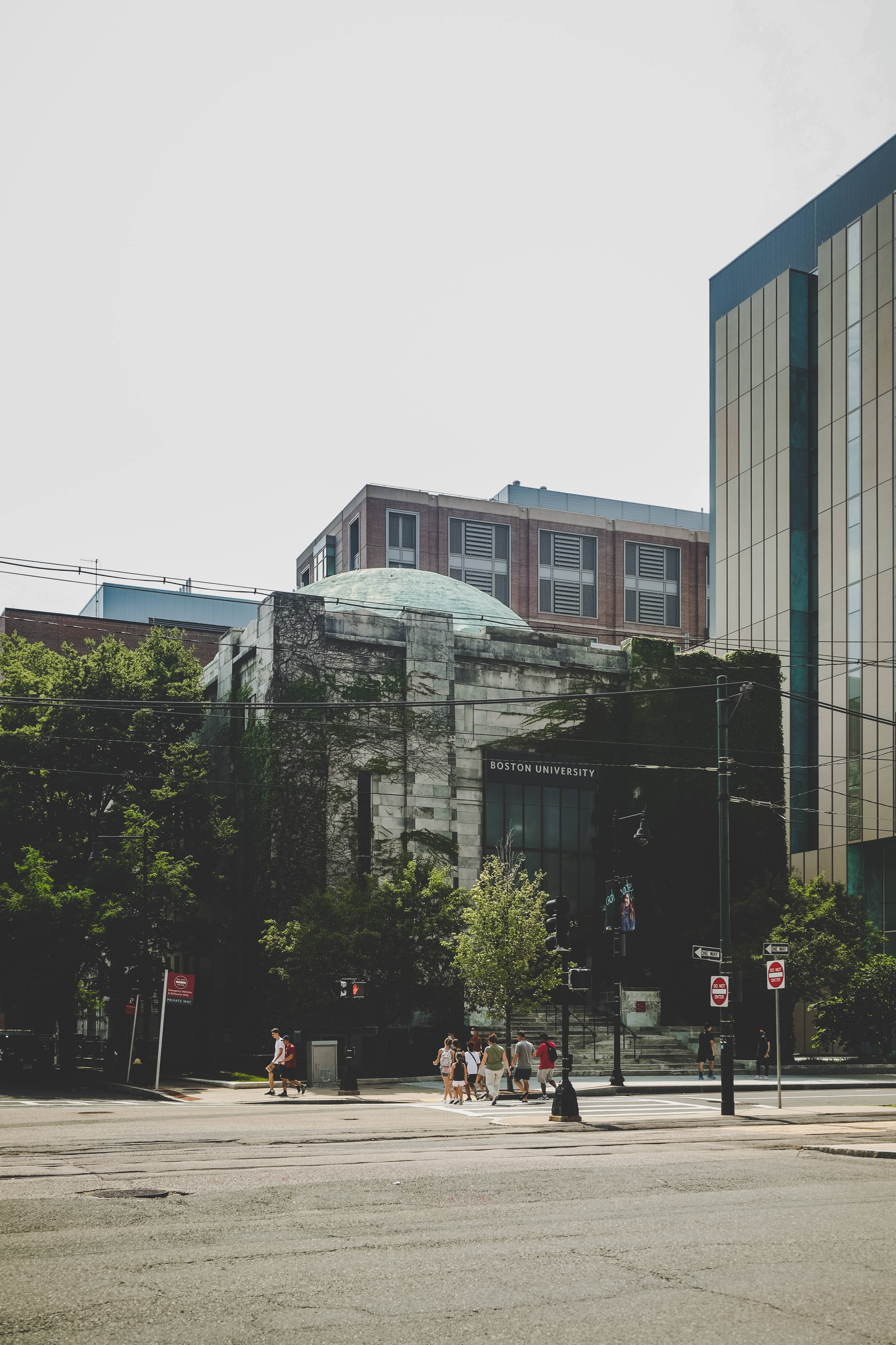 University 桌布 壁紙 — 陽光明媚的城市街景，行人在波士頓大學一棟被常春藤覆蓋的歷史建築附近過馬路。