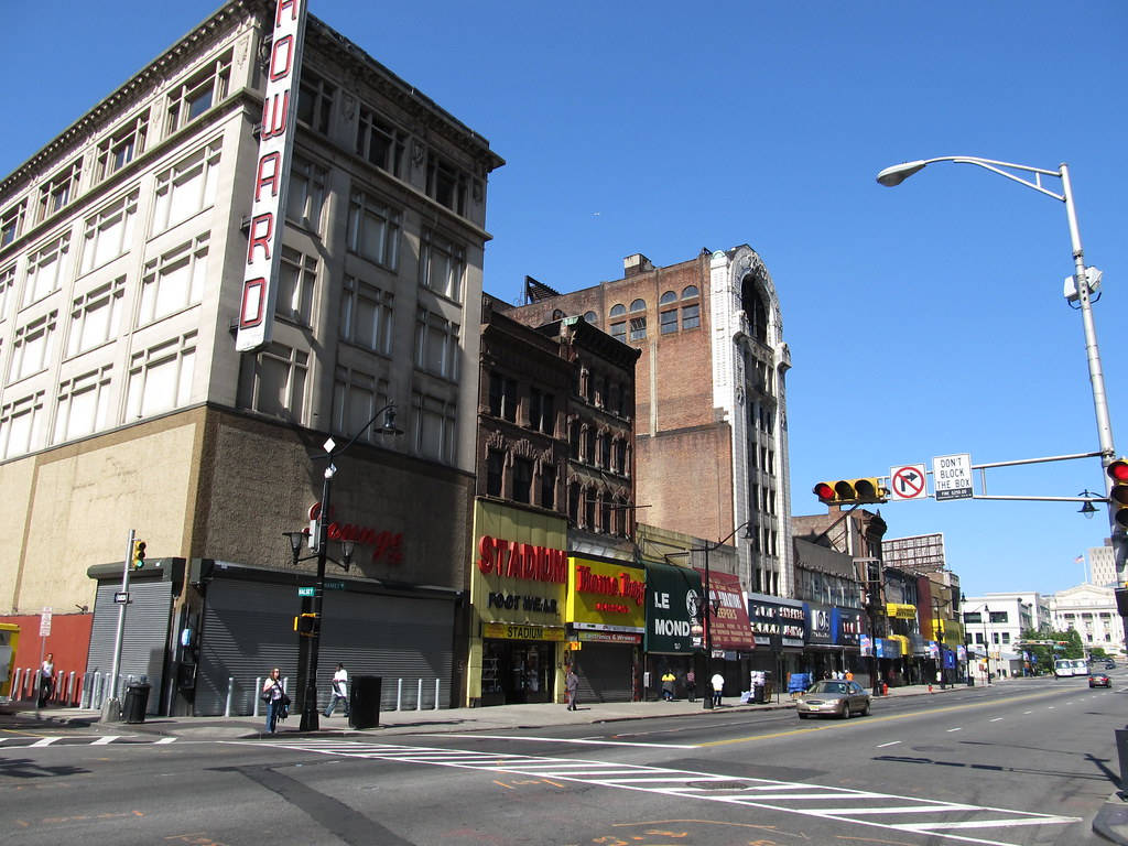 城市 桌布 壁紙 — 陽光明媚的城市街角，有復古建築、色彩繽紛的店面和人行道，在清澈的藍天下。