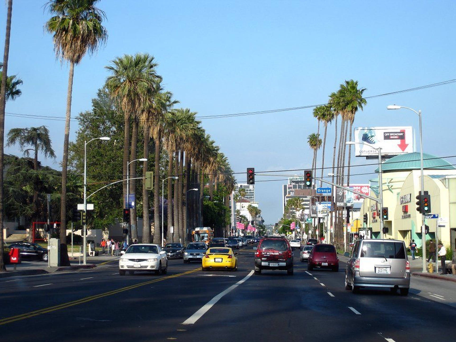 Boulevard 桌布 壁紙 — 陽光明媚的城市街道，兩旁種有高大的棕櫚樹，汽車在晴朗的藍天下行駛。