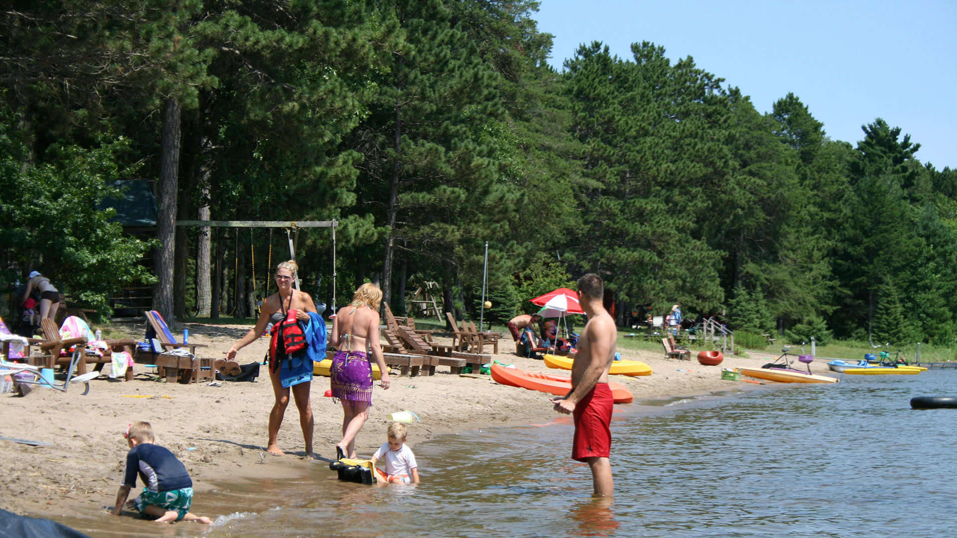 Minnesota 桌布 壁紙 — 陽光明媚的夏日，在森林湖泊沙灘上，家庭享受水上活動和皮划艇。