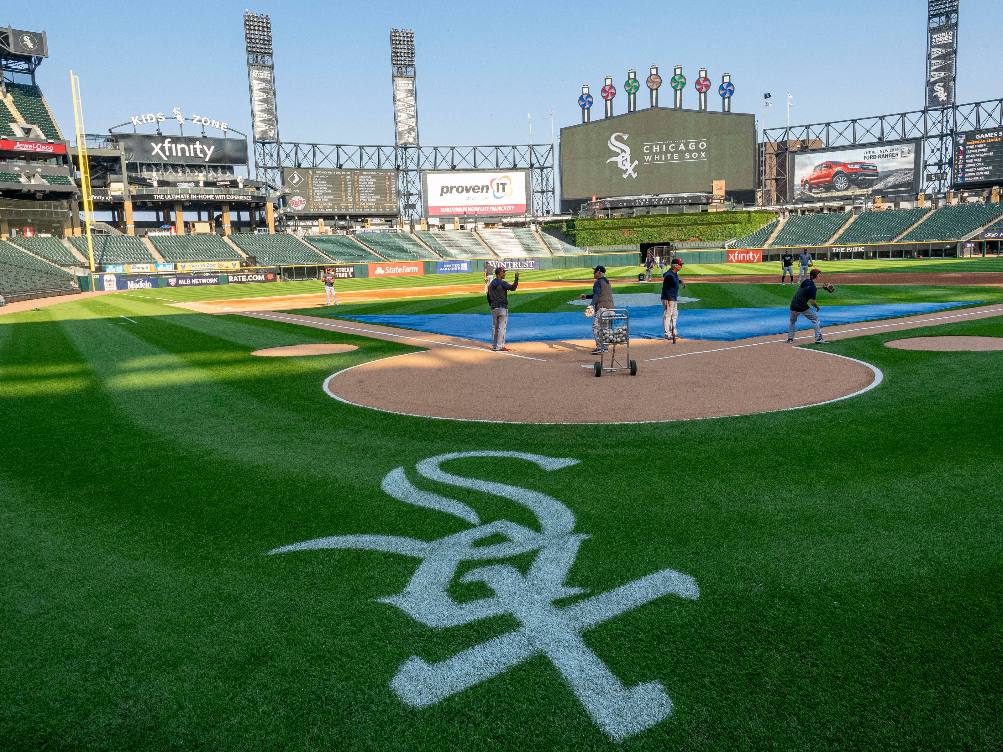 Chicago White Sox 桌布 壁紙 — 陽光明媚的棒球場，場上有球員，草地上畫有大型芝加哥白襪隊標誌。