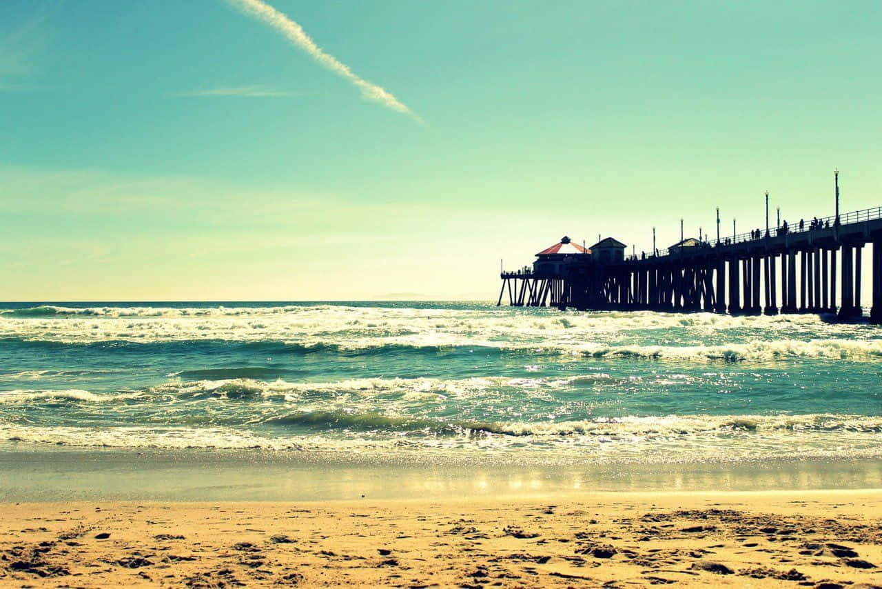 加州 桌布 壁紙 — 陽光明媚的海灘，碧綠色的海浪拍打著金色的沙灘，一條長長的木質碼頭延伸至地平線。