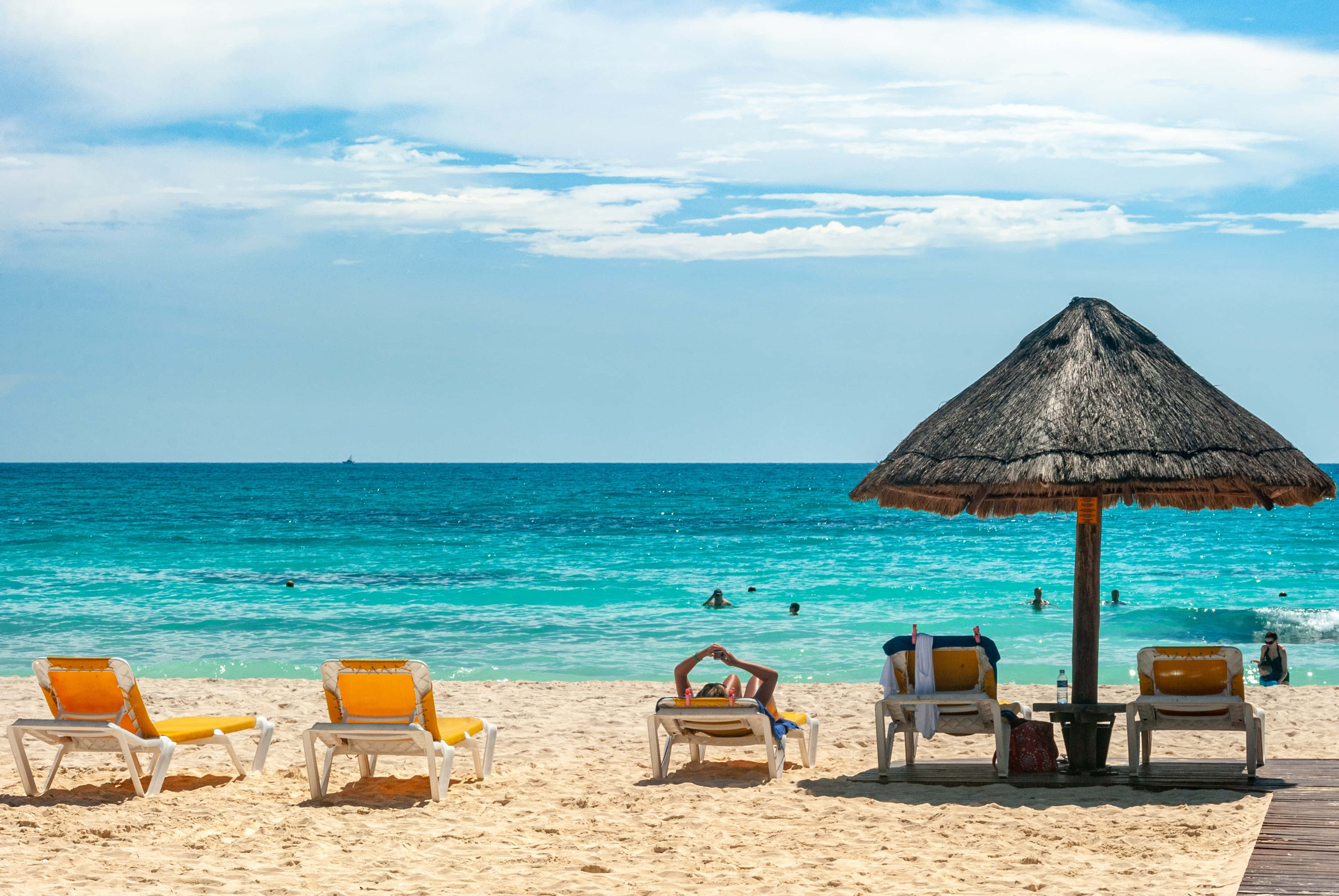 Summer Vacation 桌布 壁紙 — 陽光明媚的海灘場景，有碧綠色的海洋、茅草遮陽傘和躺椅，天空部分多雲。