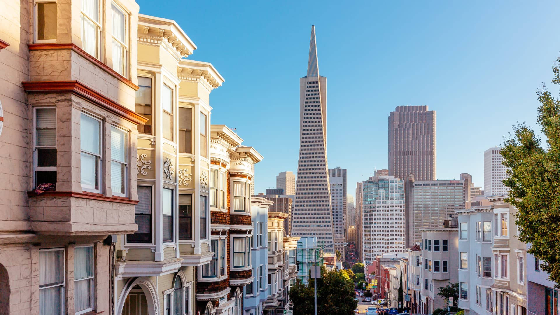 San Francisco HD 桌布 壁紙 — 陽光明媚的舊金山街道，兩旁是維多利亞式房屋，遠處是標誌性的泛美金字塔。