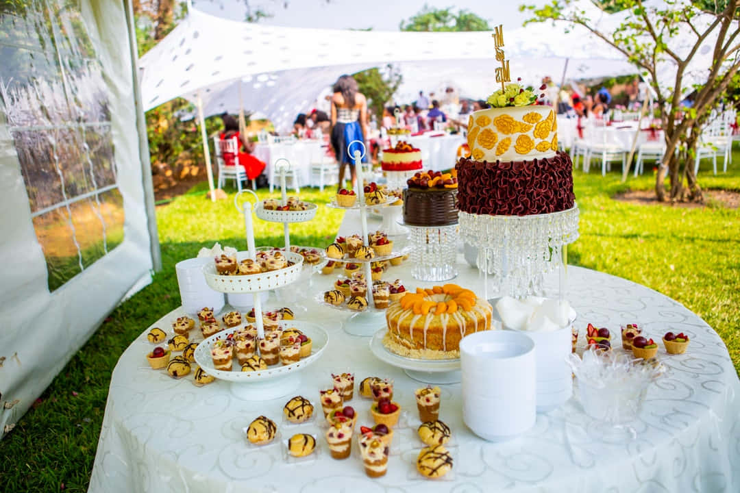 Birthday Party 桌布 壁紙 — 陽光明媚的草坪上，白色天篷下擺滿了多層蛋糕、糕點和杯子蛋糕的奢華戶外婚禮甜點桌。
