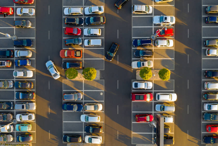汽車 桌布 壁紙 — 陽光普照的停車場鳥瞰圖，整齊的停車位之間，一排排色彩繽紛的汽車投下長長的影子。