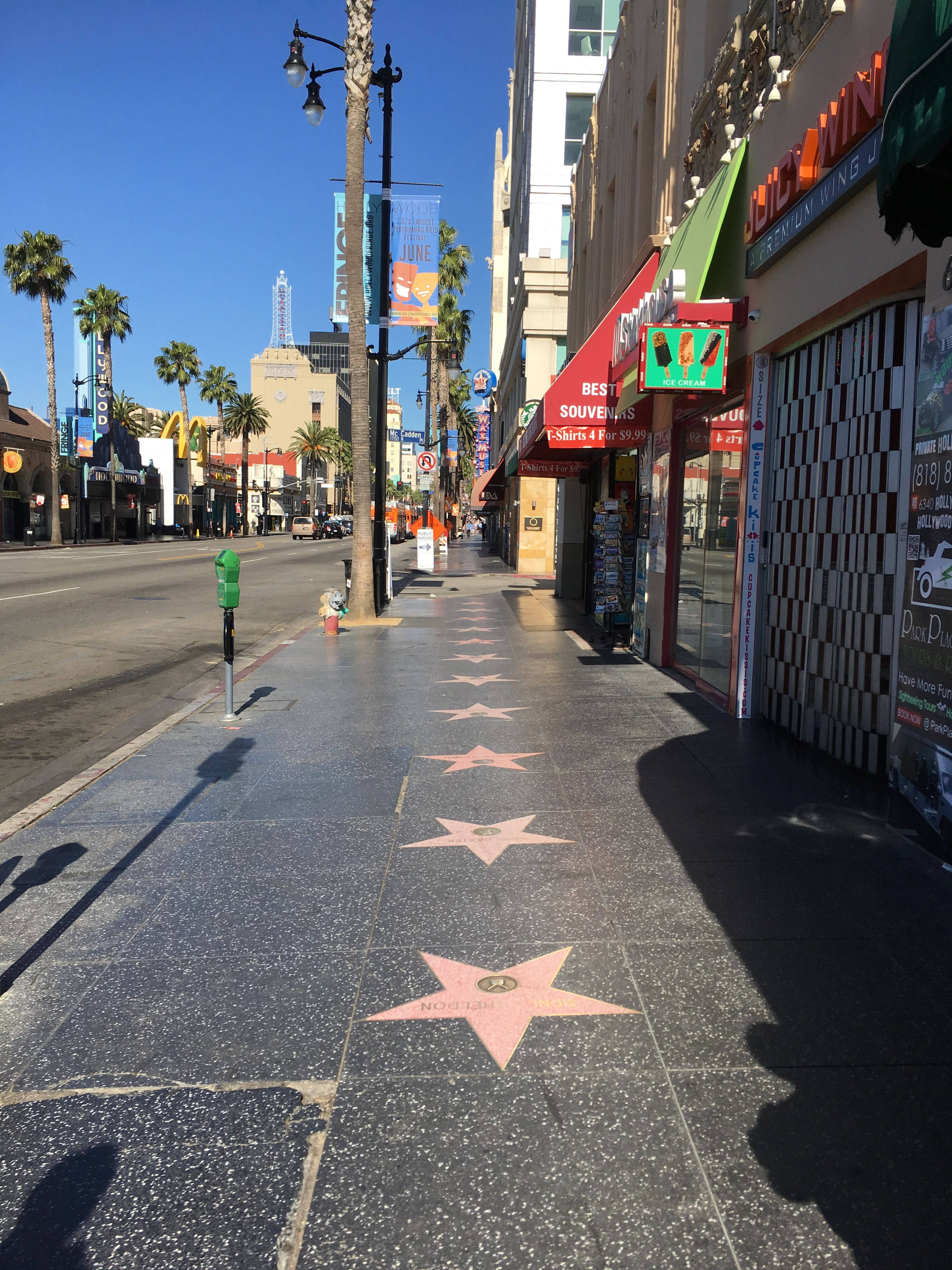 hollywood street 桌布 壁紙 — 陽光普照的好萊塢星光大道人行道，黑色磨石子中鑲嵌粉紅色星星，天空清澈湛藍。