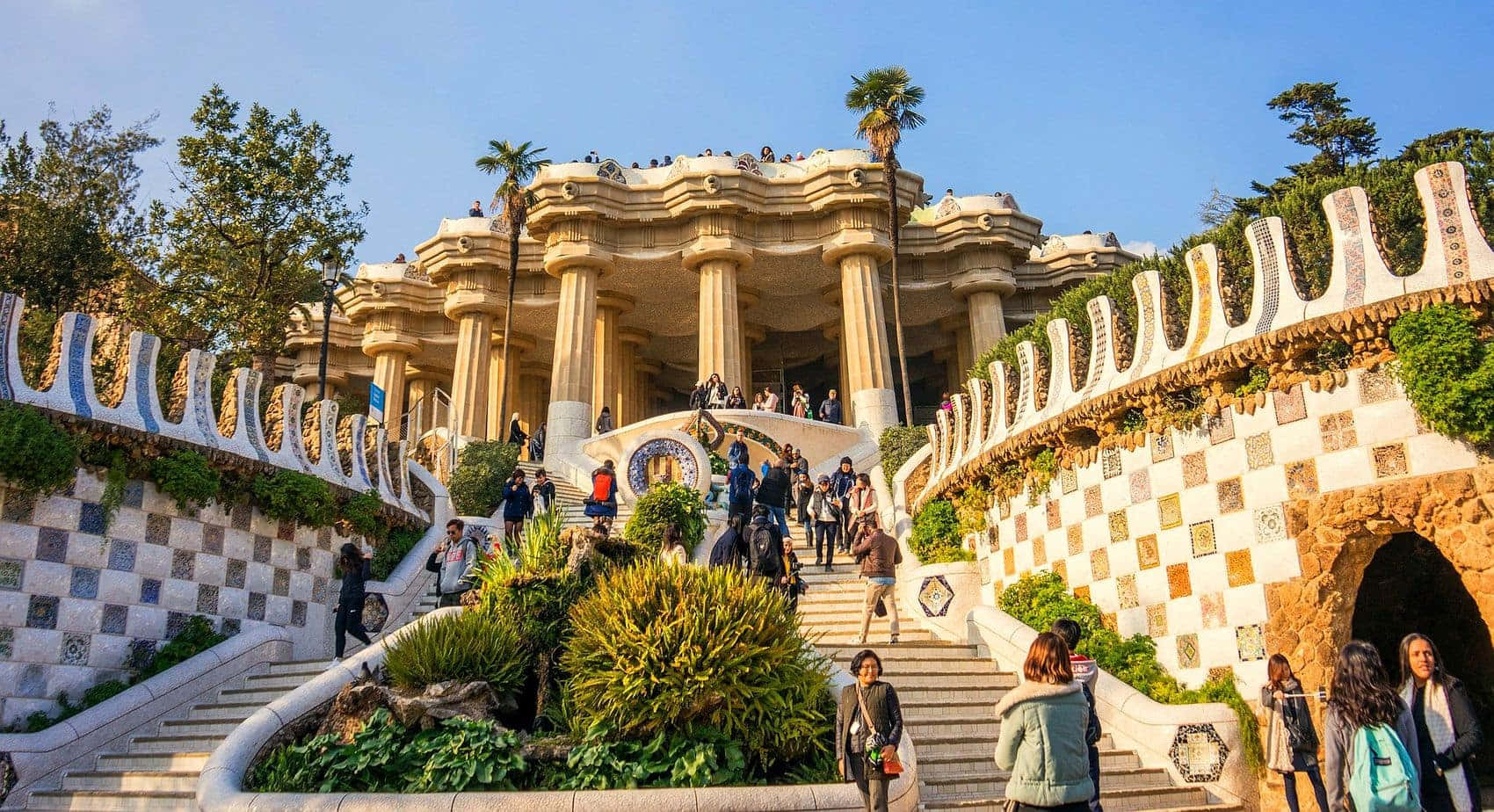 Barcelona 桌布 壁紙 — 陽光普照的宏偉樓梯，飾有華麗瓷磚牆壁和茂密綠植，通往晴朗藍天下的一座古典亭閣。
