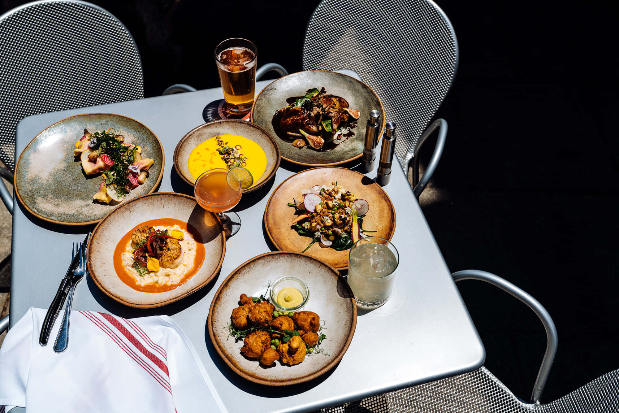 Beautiful Food 桌布 壁紙 — 陽光普照的戶外餐桌，擺放著五道色彩繽紛的美食佳餚和飲品，周圍是金屬網椅。