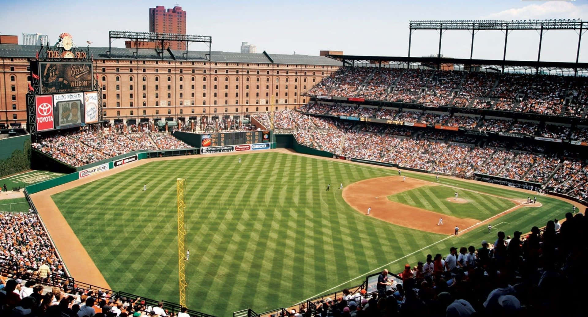 Baseball Stadium 桌布 壁紙 — 陽光普照的棒球場鳥瞰圖，場內擠滿球迷在充滿活力的綠色場地上觀看比賽。