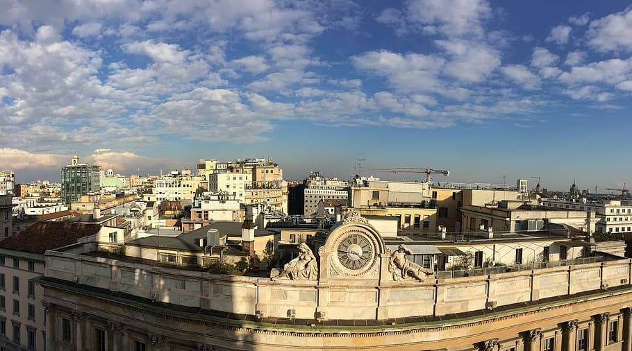 Milan 桌布 壁紙 — 陽光普照的歐洲城市全景，擁有華麗的屋頂和充滿蓬鬆白雲的戲劇性藍天。
