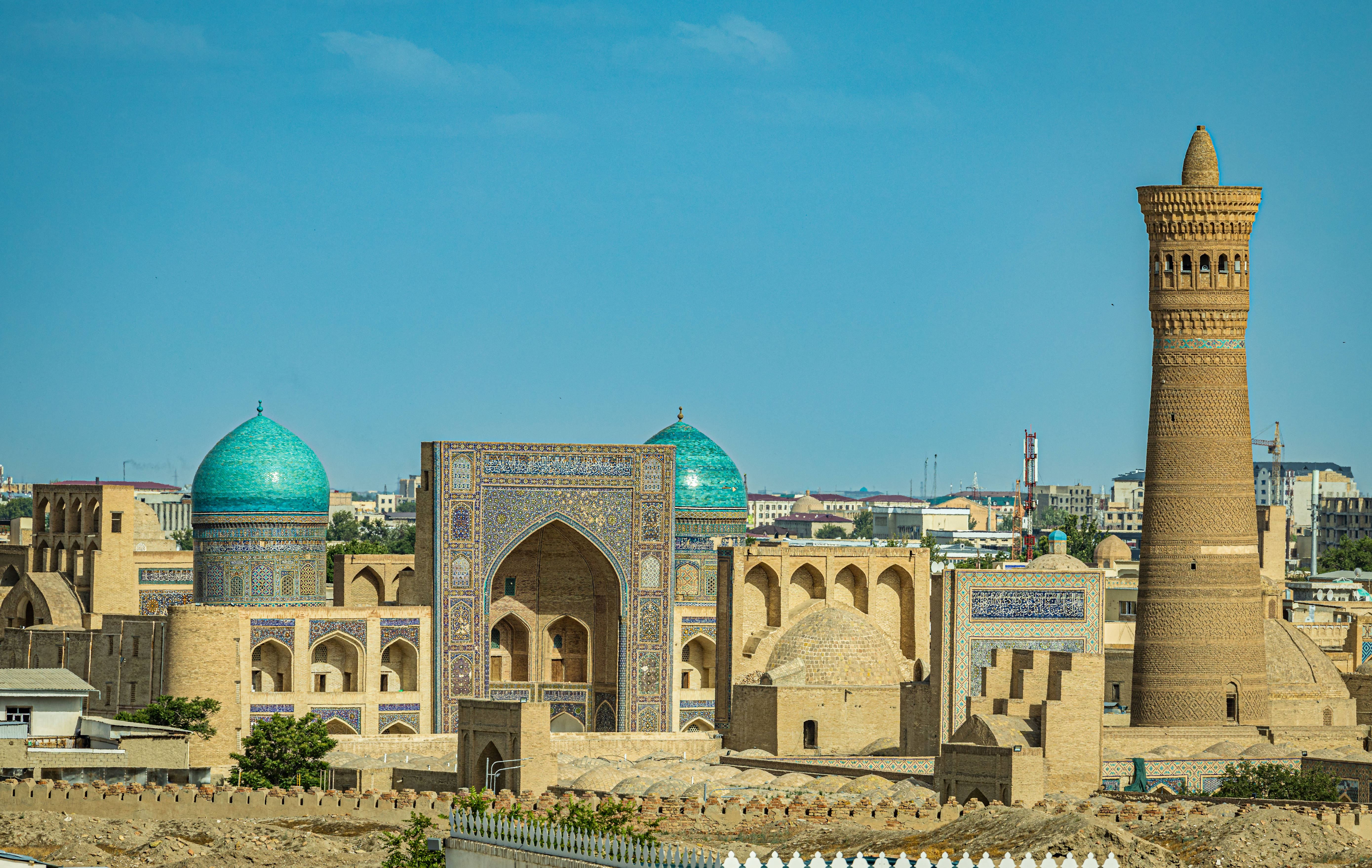 Uzbekistan 桌布 壁紙 — 陽光普照的歷史伊斯蘭建築，擁有藍綠色圓頂和高磚砌宣禮塔，映襯著清澈的藍天。