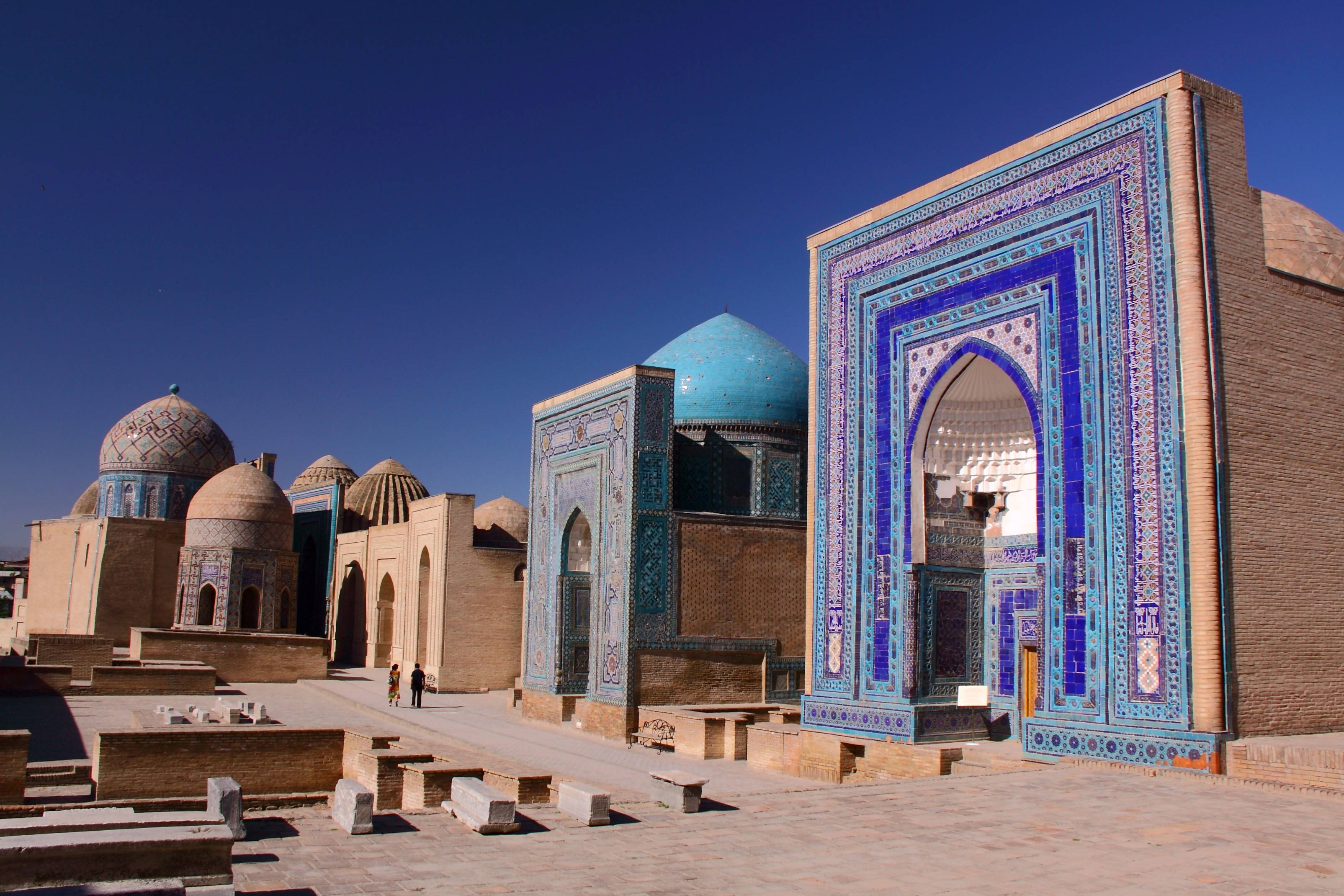 Uzbekistan 桌布 壁紙 — 陽光普照的歷史伊斯蘭建築，擁有鮮豔的藍色瓷磚拱門和圓頂，在清澈的蔚藍天空下。