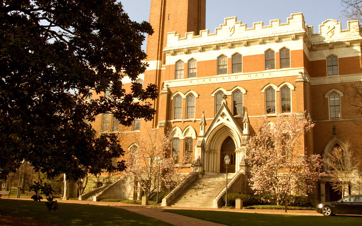  壁紙 — 陽光普照的歷史磚造建築Kirkland Hall，哥德式拱門與盛開的粉紅樹木襯托著宏偉的石階梯。