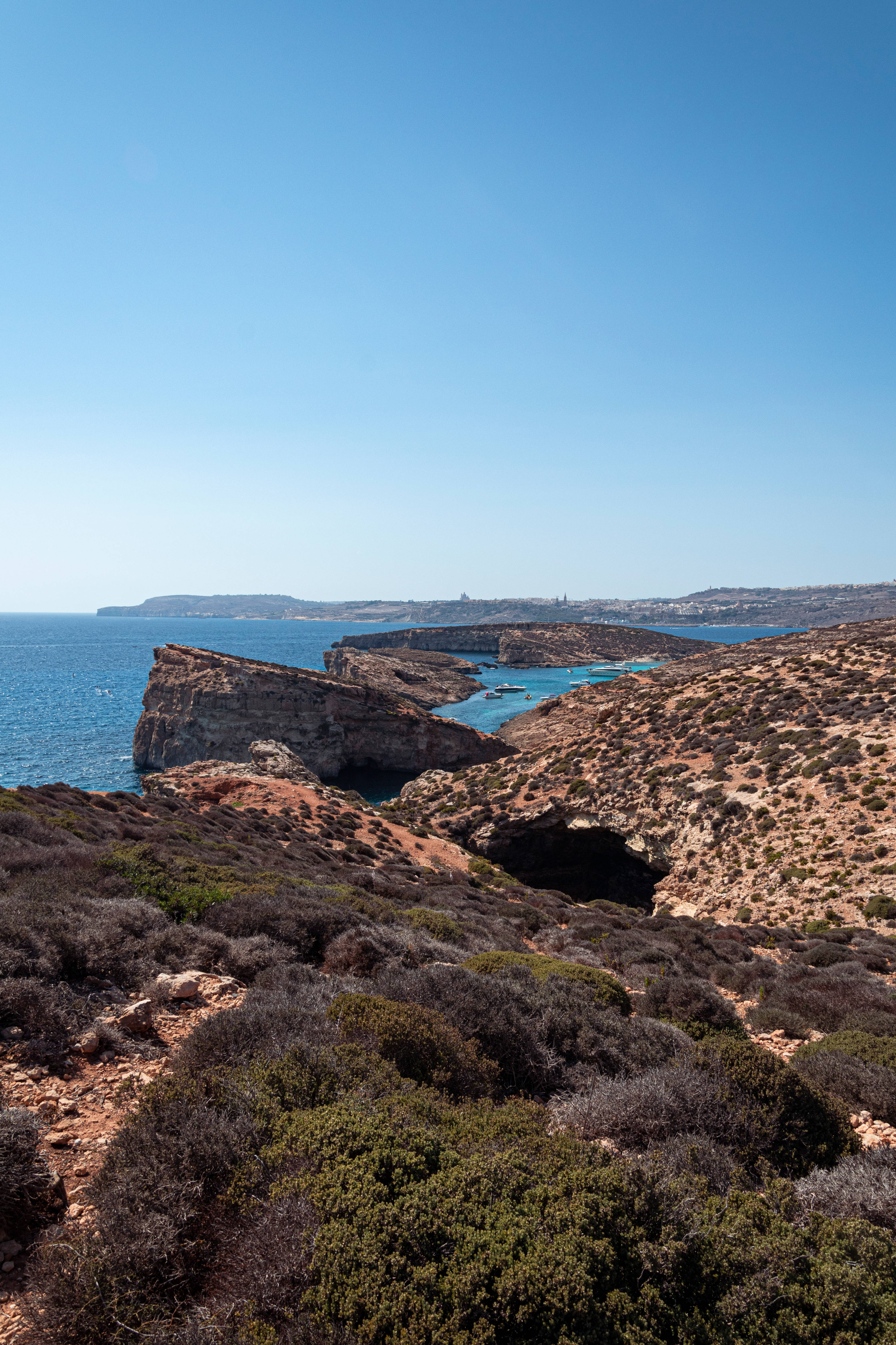 Malta 桌布 壁紙 — 陽光普照的海岸懸崖，碧綠海水與稀疏灌木，襯托清澈藍天。