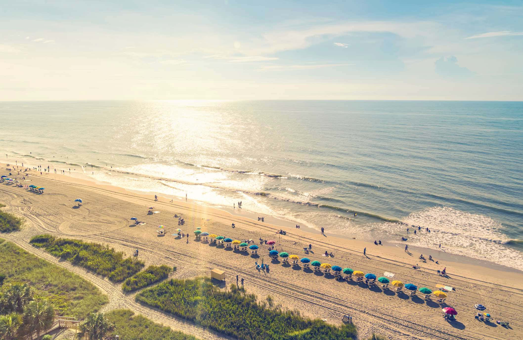 Myrtle Beach 桌布 壁紙 — 陽光普照的海灘鳥瞰圖，色彩繽紛的遮陽傘沿著海岸線排列，海浪輕輕拍打。
