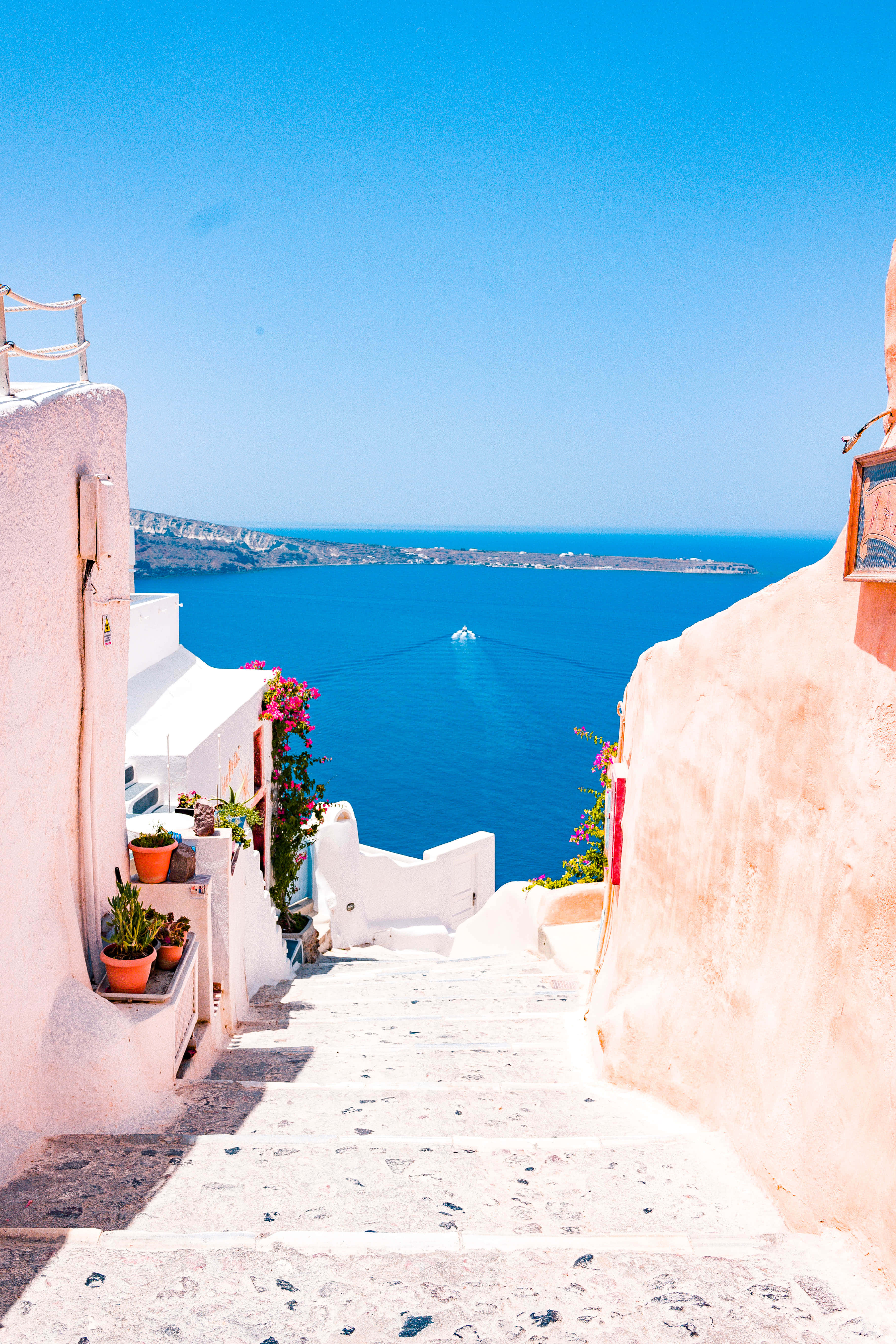 Santorini 桌布 壁紙 — 陽光普照的白色石階通往充滿活力的藍色愛琴海，遠處有一艘小船，天空晴朗。