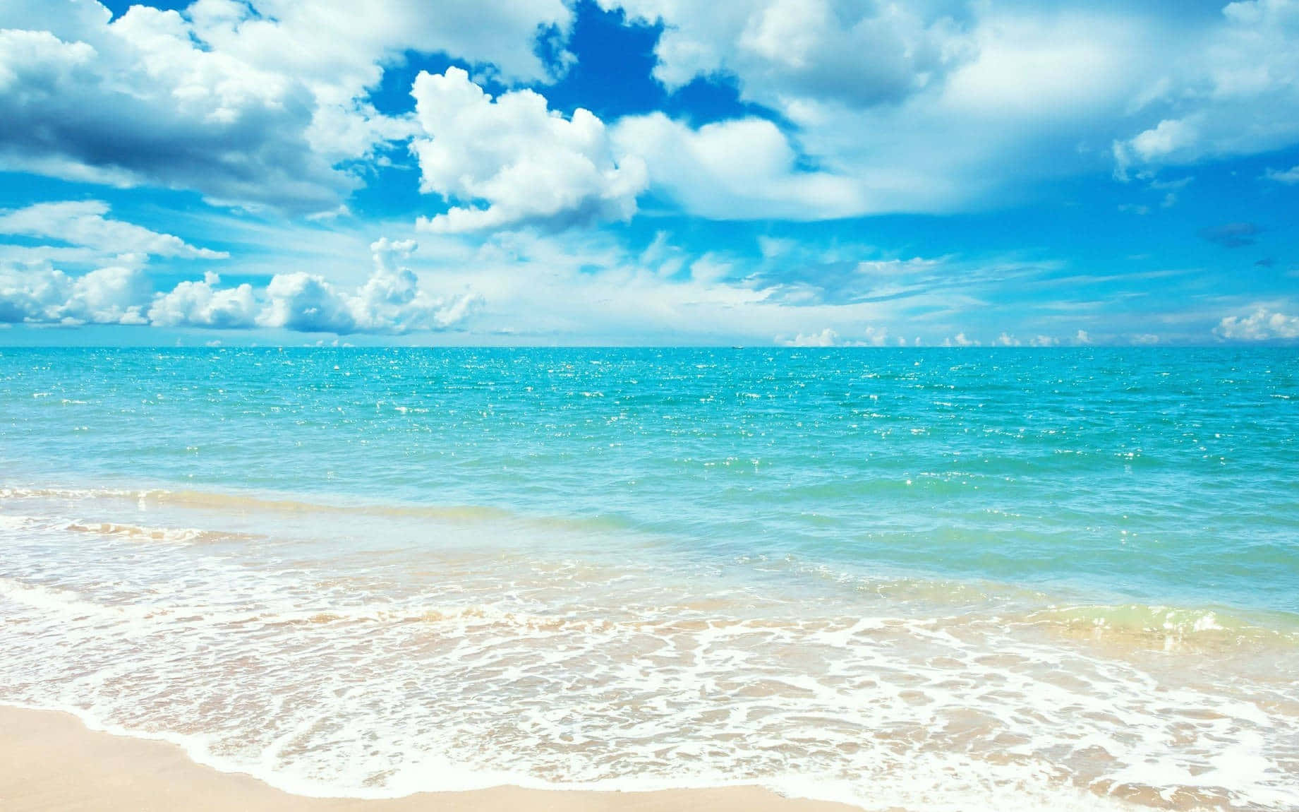 Cute Tropical 桌布 壁紙 — 陽光普照的碧綠海浪輕輕地拍打著金色的沙灘，上方是充滿蓬鬆白雲的湛藍天空。