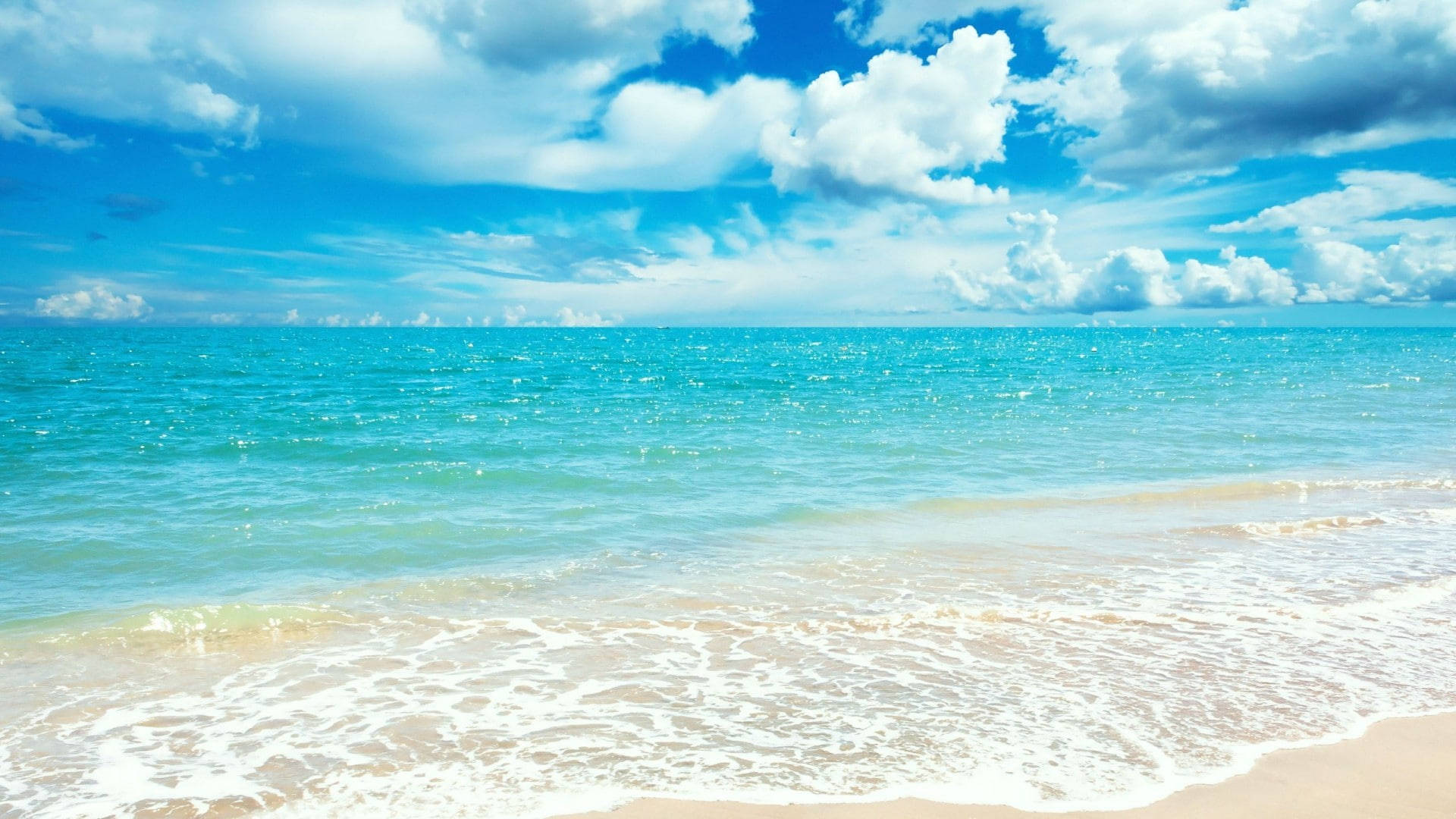 夏天 桌布 壁紙 — 陽光普照的碧綠海浪輕輕拍打著金色沙灘，上方是點綴著蓬鬆白雲的湛藍天空。